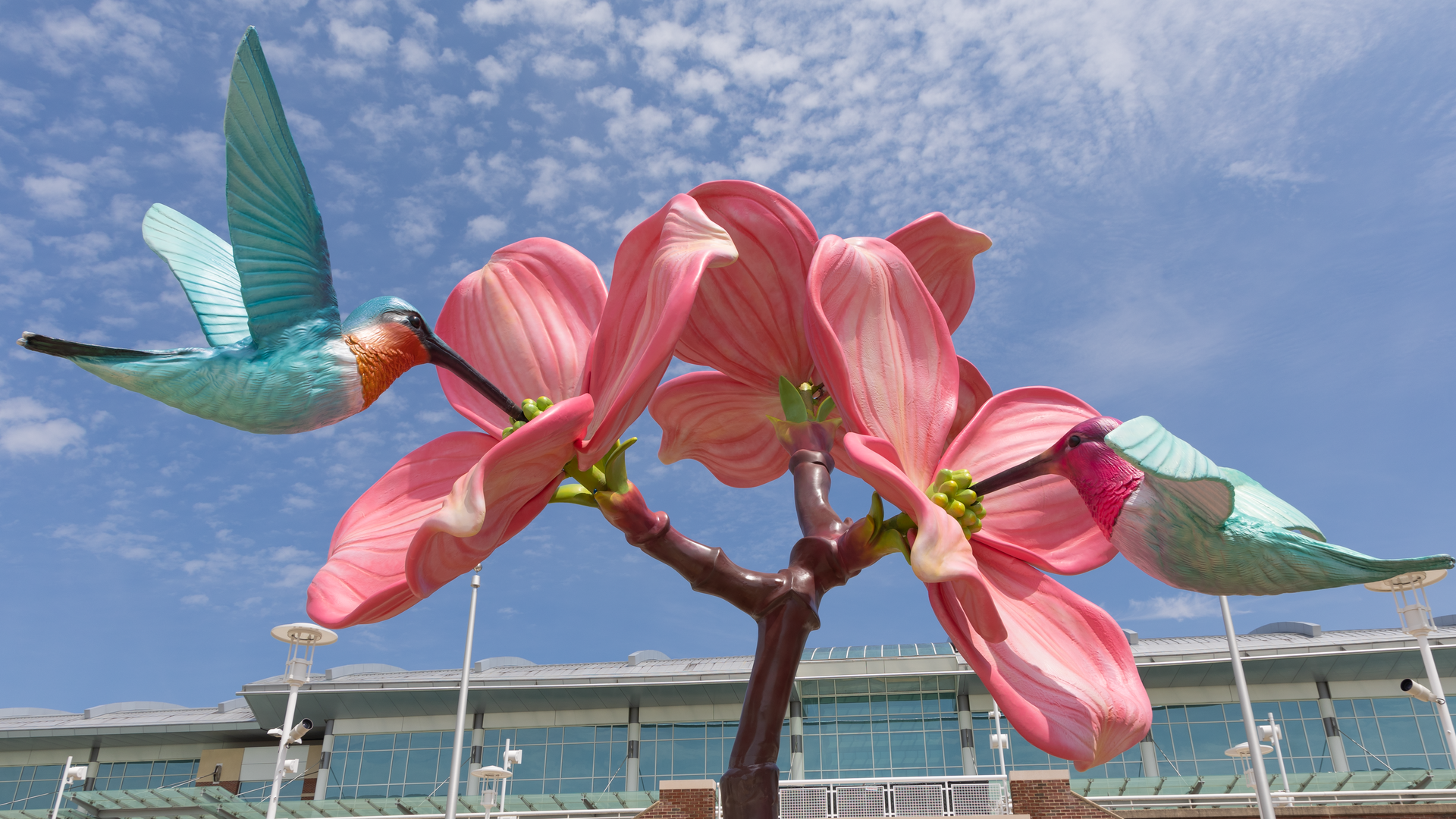 A pink flower sculpture with two blue-green hummingbirds drinking from it