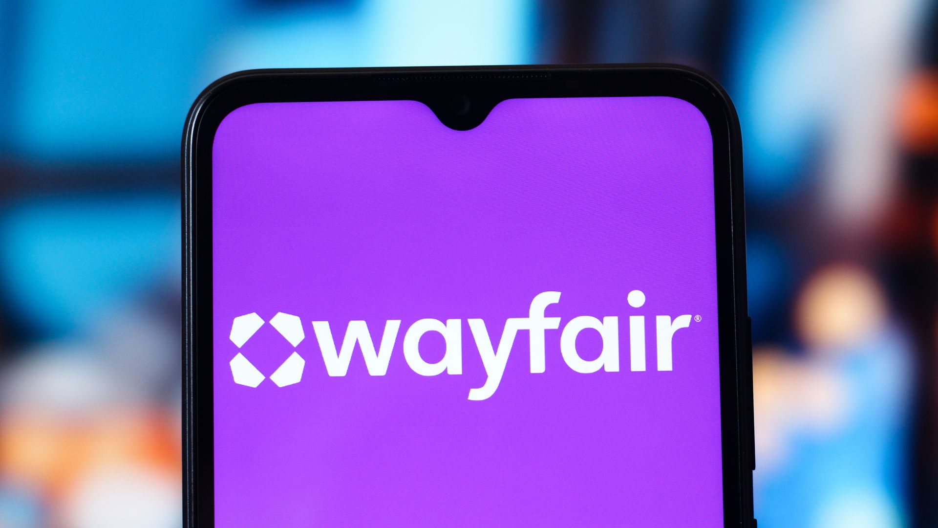 Close-up of a smartphone displaying a purple screen with the white Wayfair logo and hexagon icon, framed by a black border against a blurred blue background.