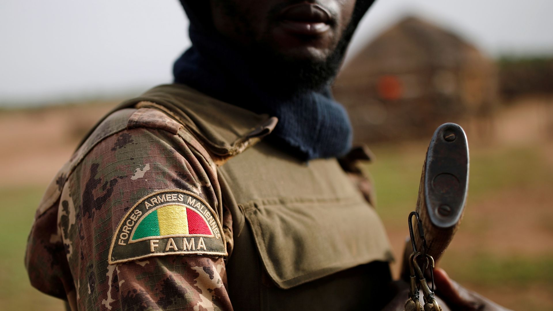 In this image, an armed soldier holds a gun and his sleeve is decorated with a patch that bears the Mali flag