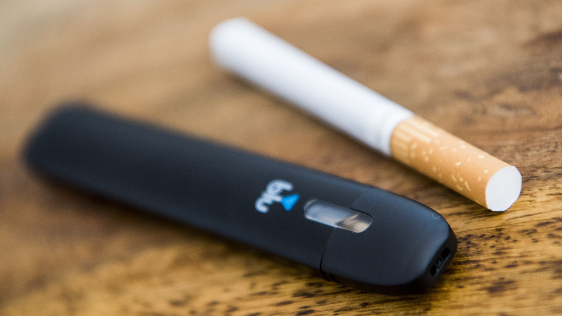 Photo of an e-cigarette next to tobacco combustible cigarette on table