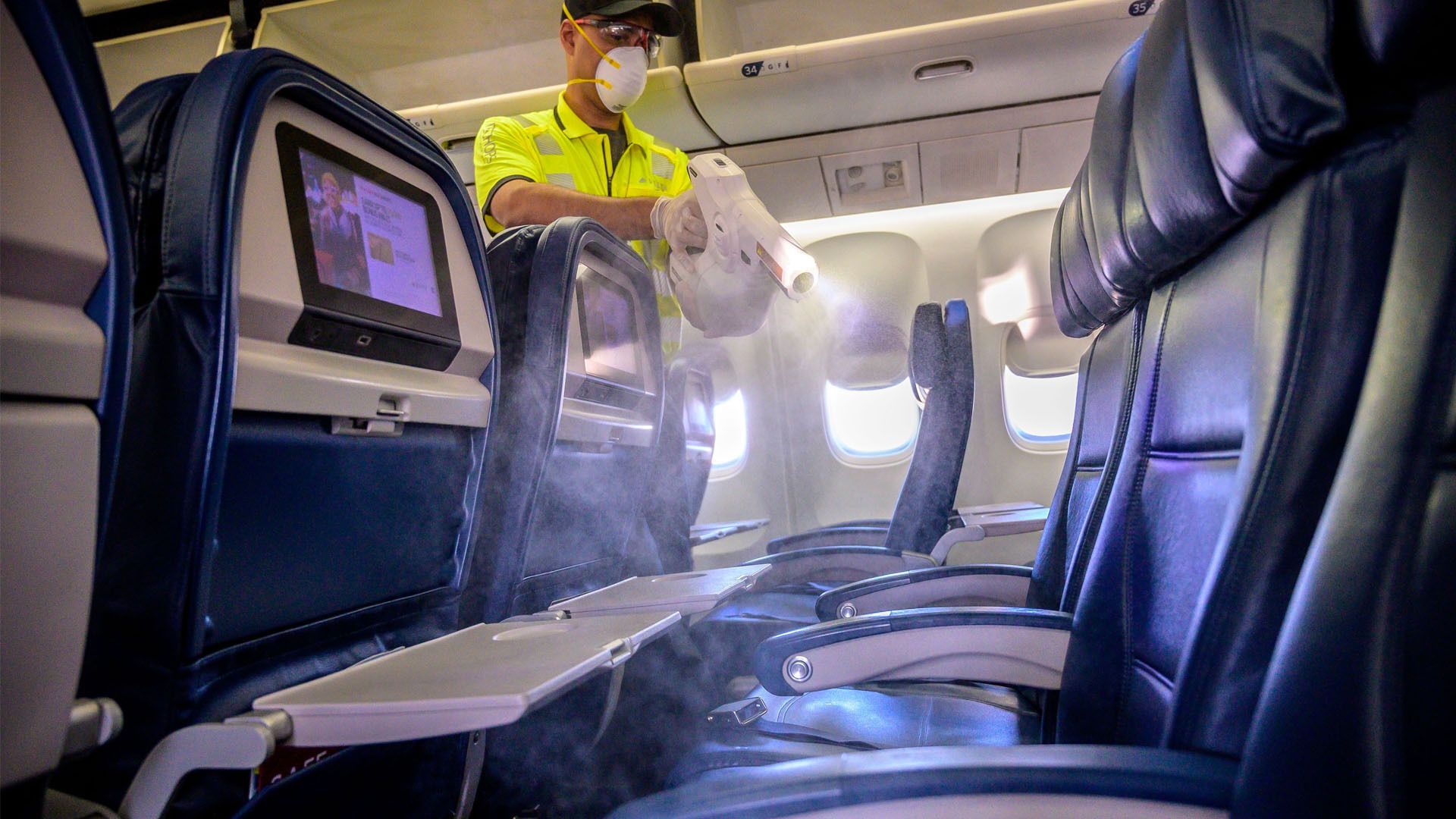 Image of Delta Air Lines worker spraying disinfectant on passenger seats.