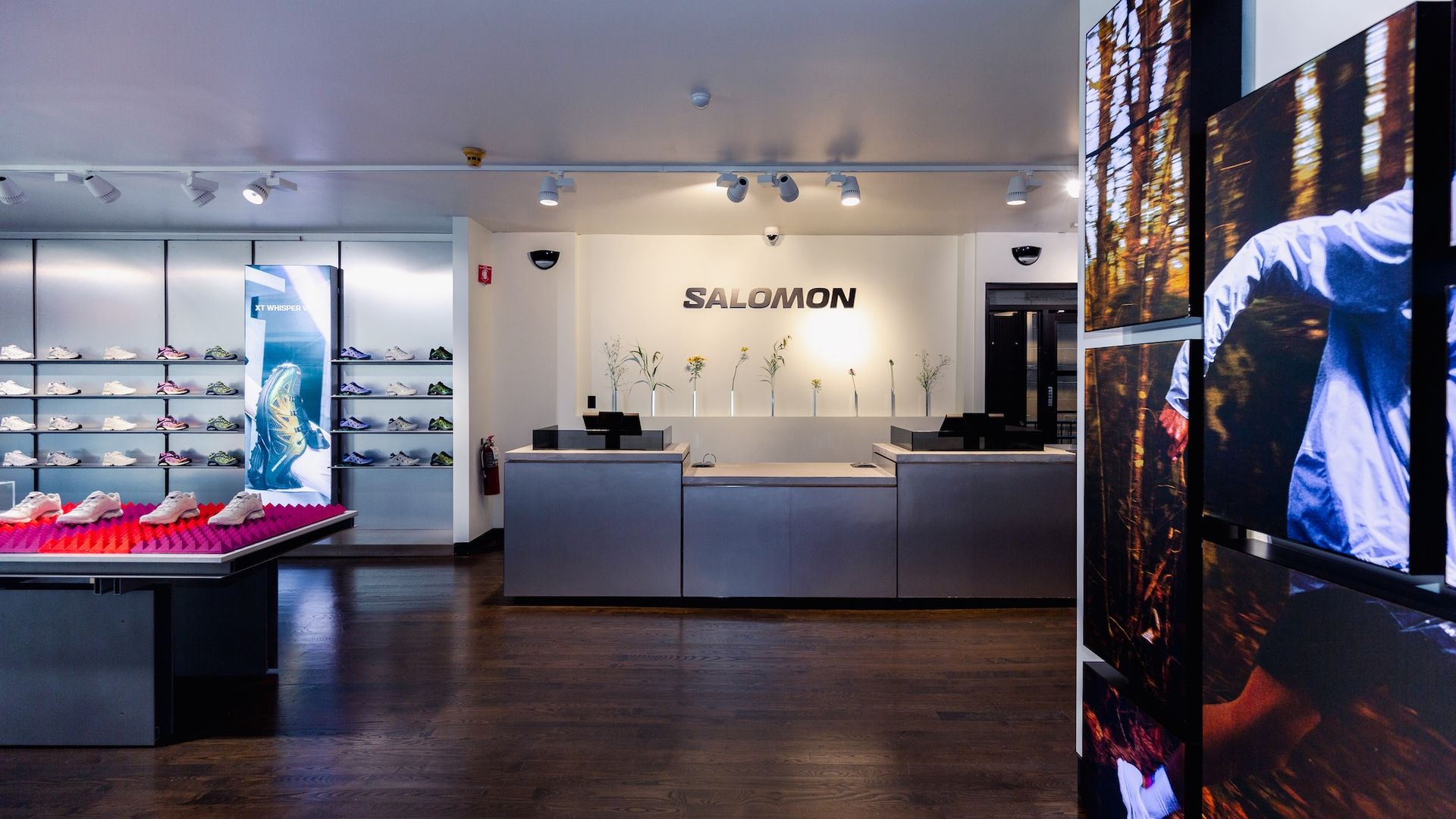 Inside a store with a wall of running shoes, a counter with a sign Salomon in all cpas and an image of a person running on the wall.