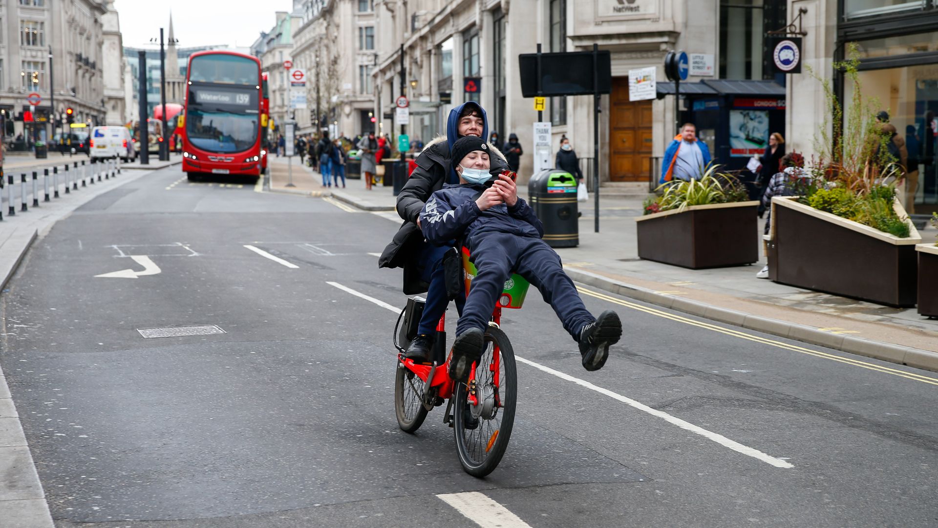 People riding a single bike together through an empty street.