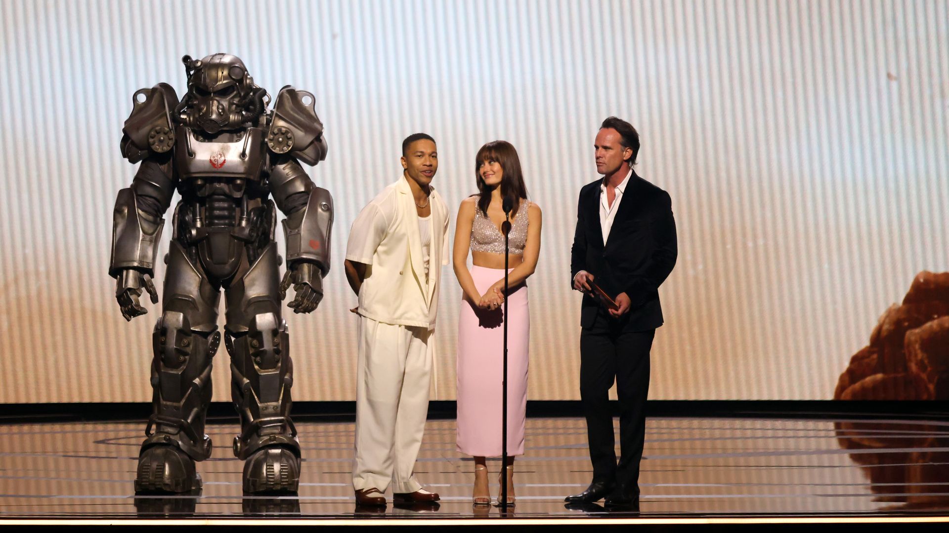 Photo of three people on stage alongside someone in armer, standing behind a microphone