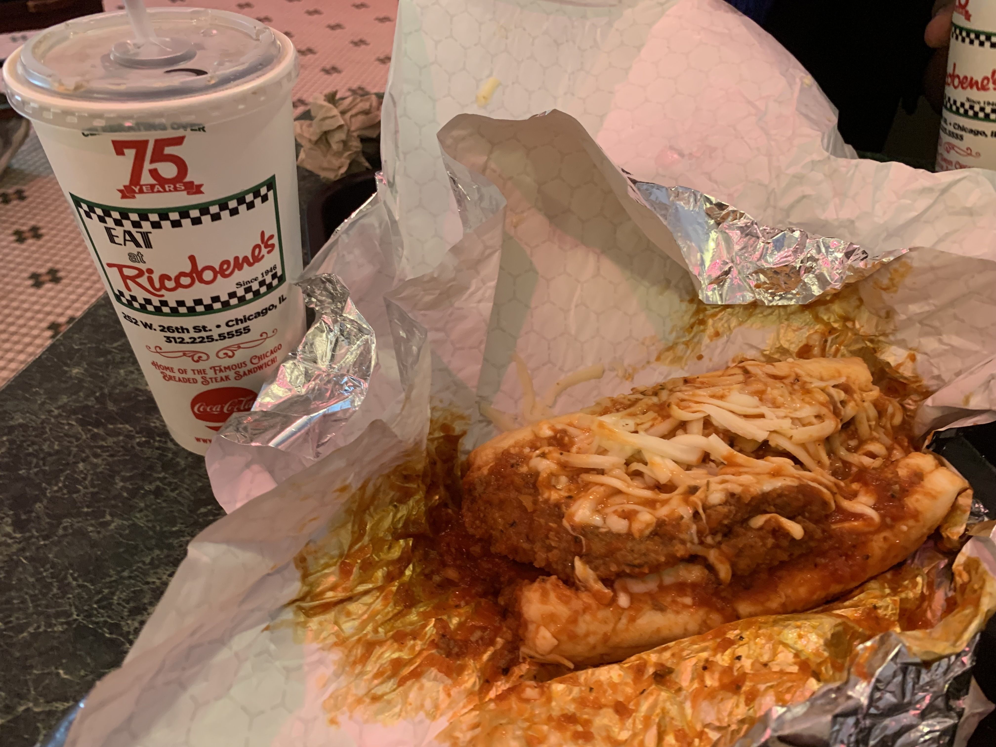 A breaded steak sandwich smothered with marinara sauce and melted cheese on top, unwrapped messily in foil.