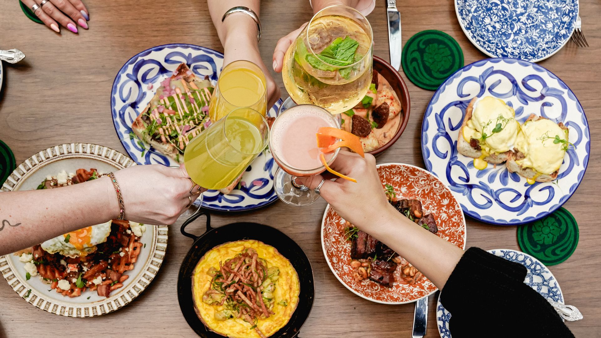 hands cheersing with cocktails over a brunch spread