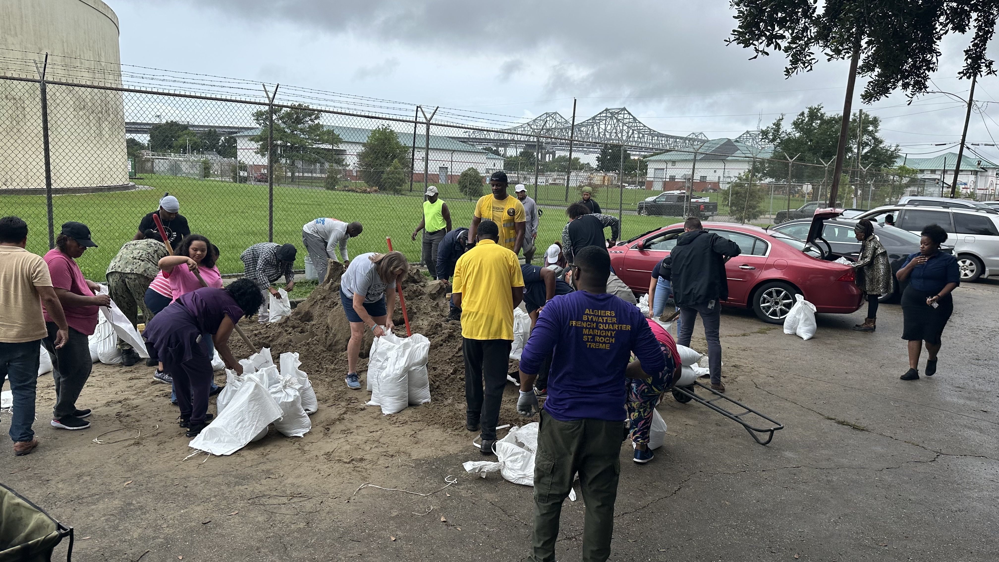 About two dozen people fill sandbags under grey skies with the Crescent City Connection in the background.