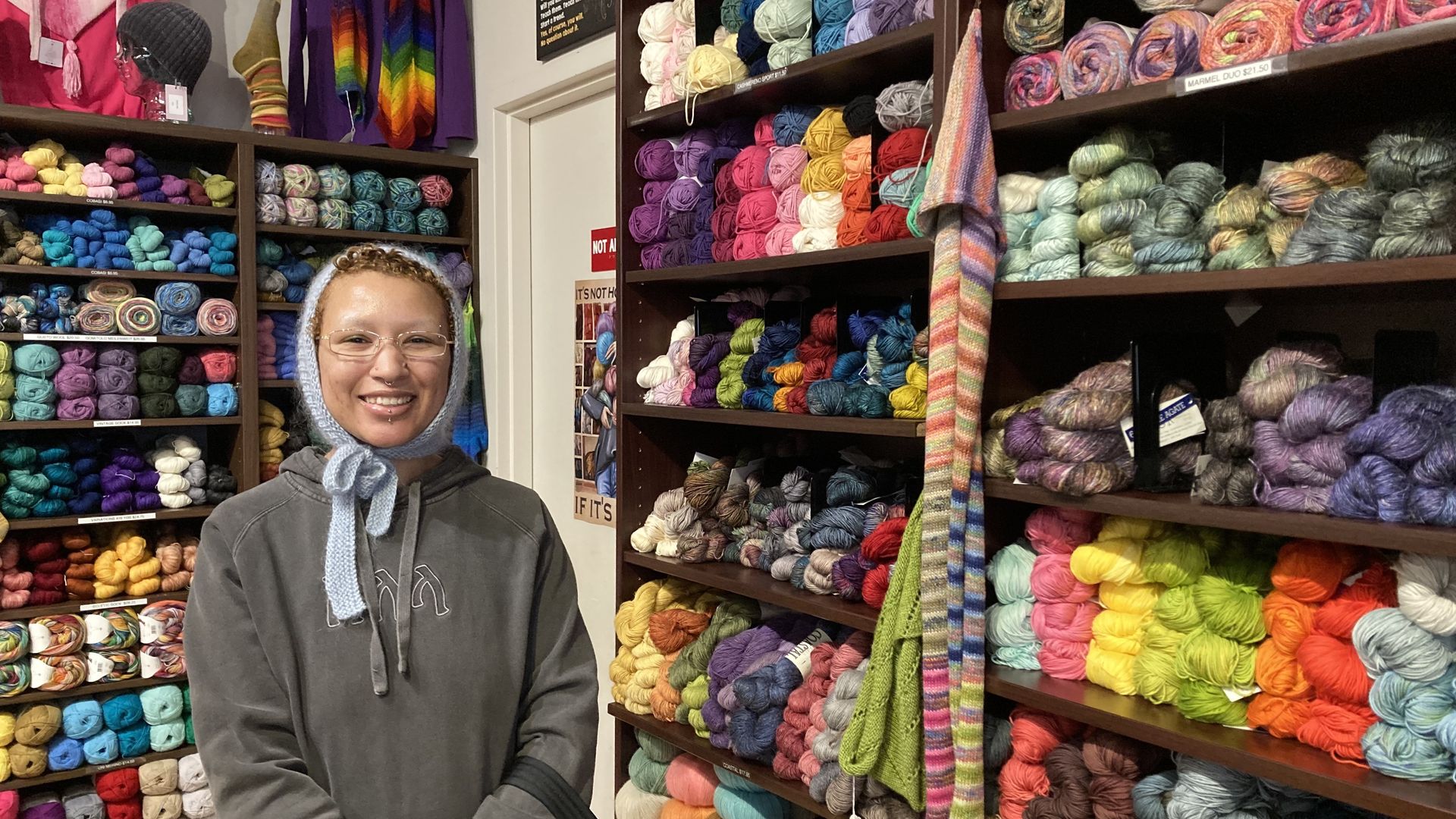A young knitter shops for yarn in a Seattle yarn store wearing a hat she made. 