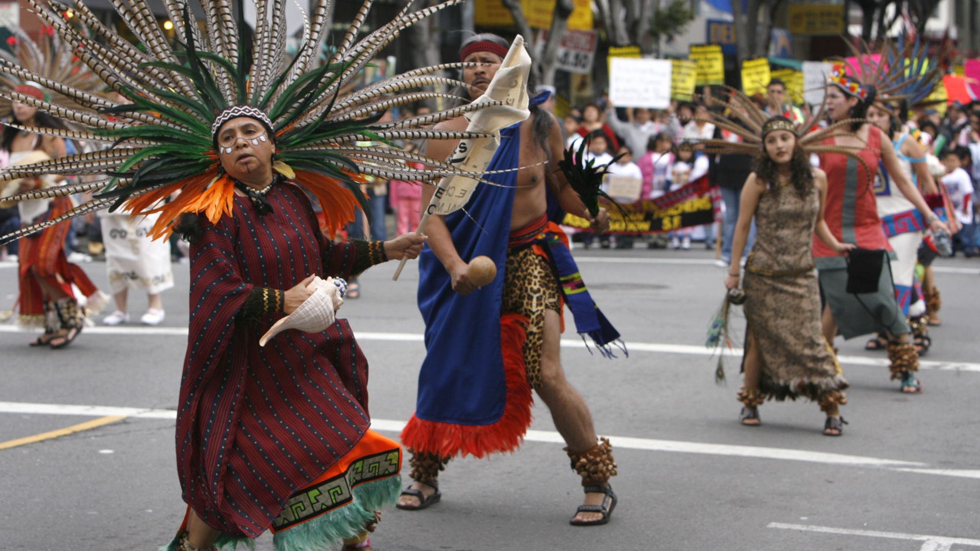 Photo of Aztec dancers dressed in traditional garb performing at a parade