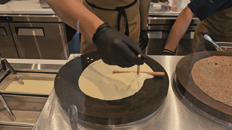 A video of a man spreading crepe batter on a griddle.