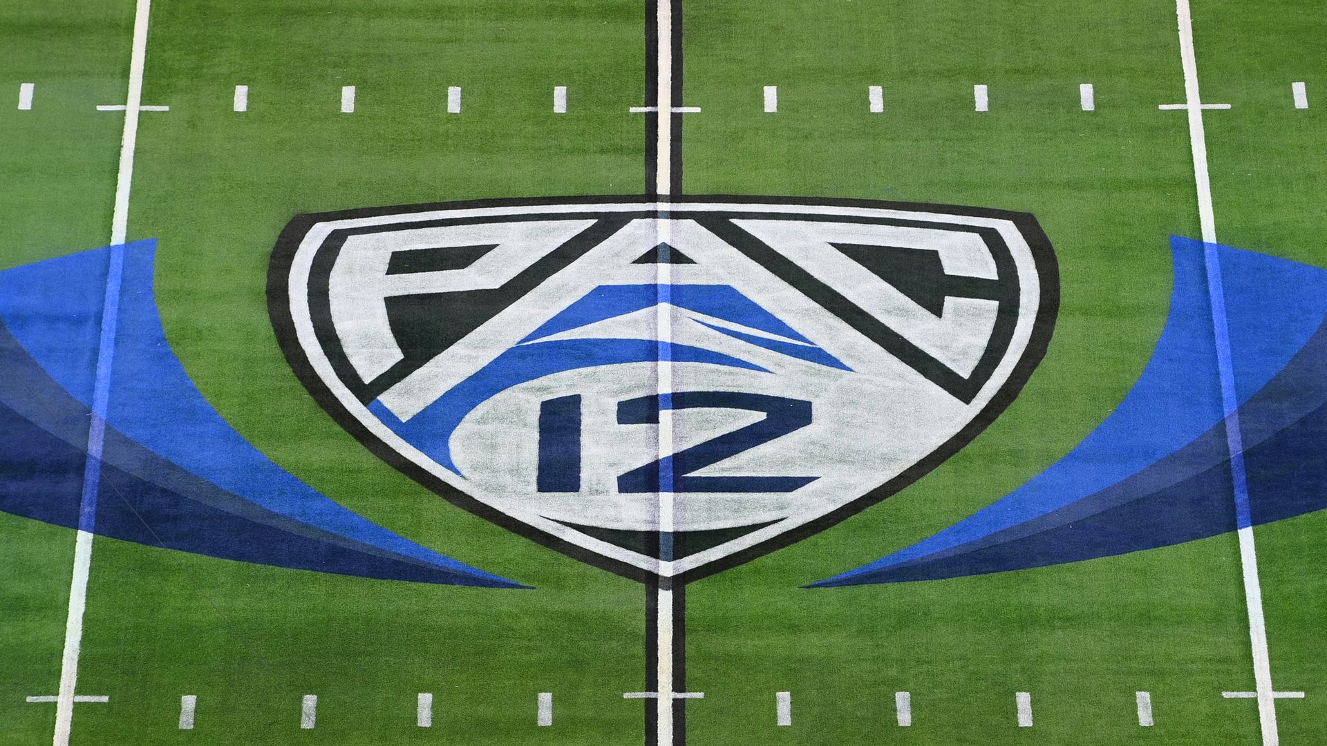 The middle of a football field with a blue and white shield shaped logo on it that say Pac 12.