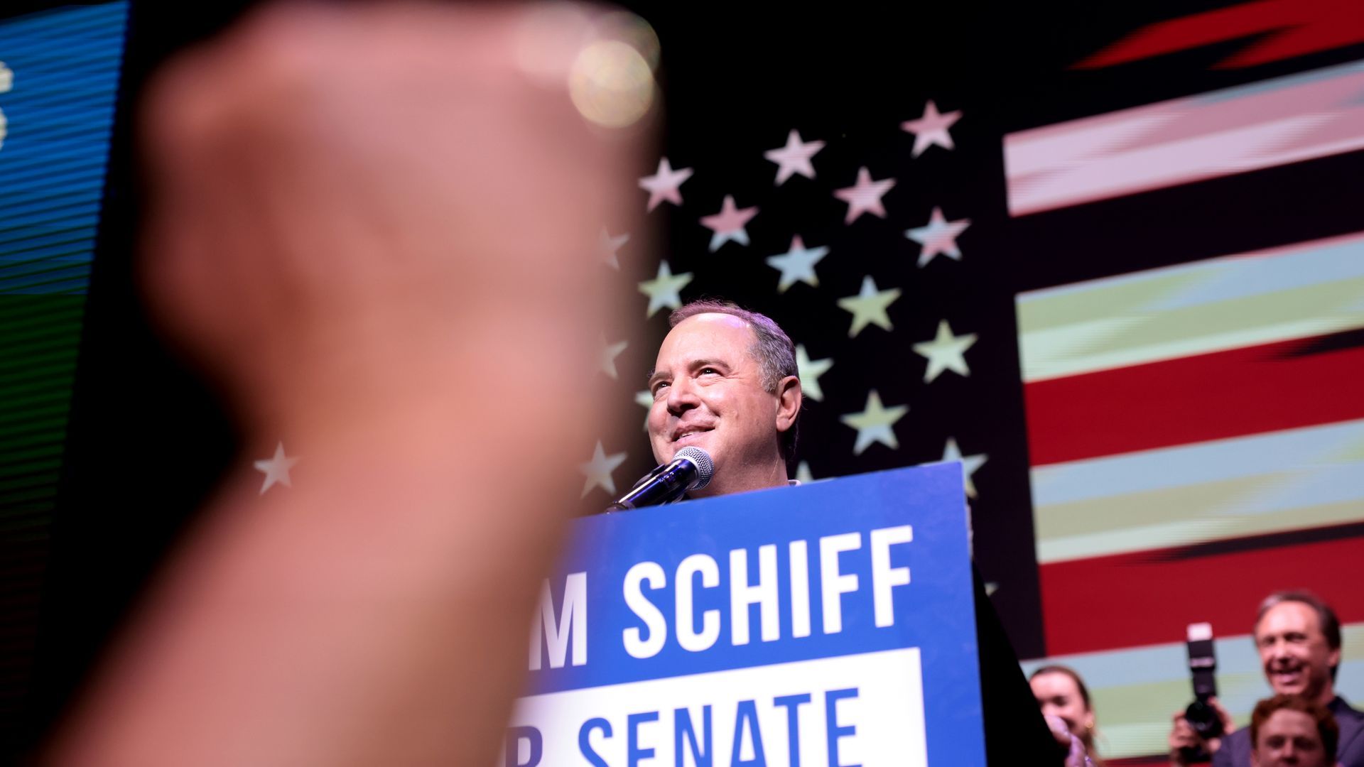 U.S. Senate candidate Adam Schiff stands a podium with a giant American flag displayed behind him.