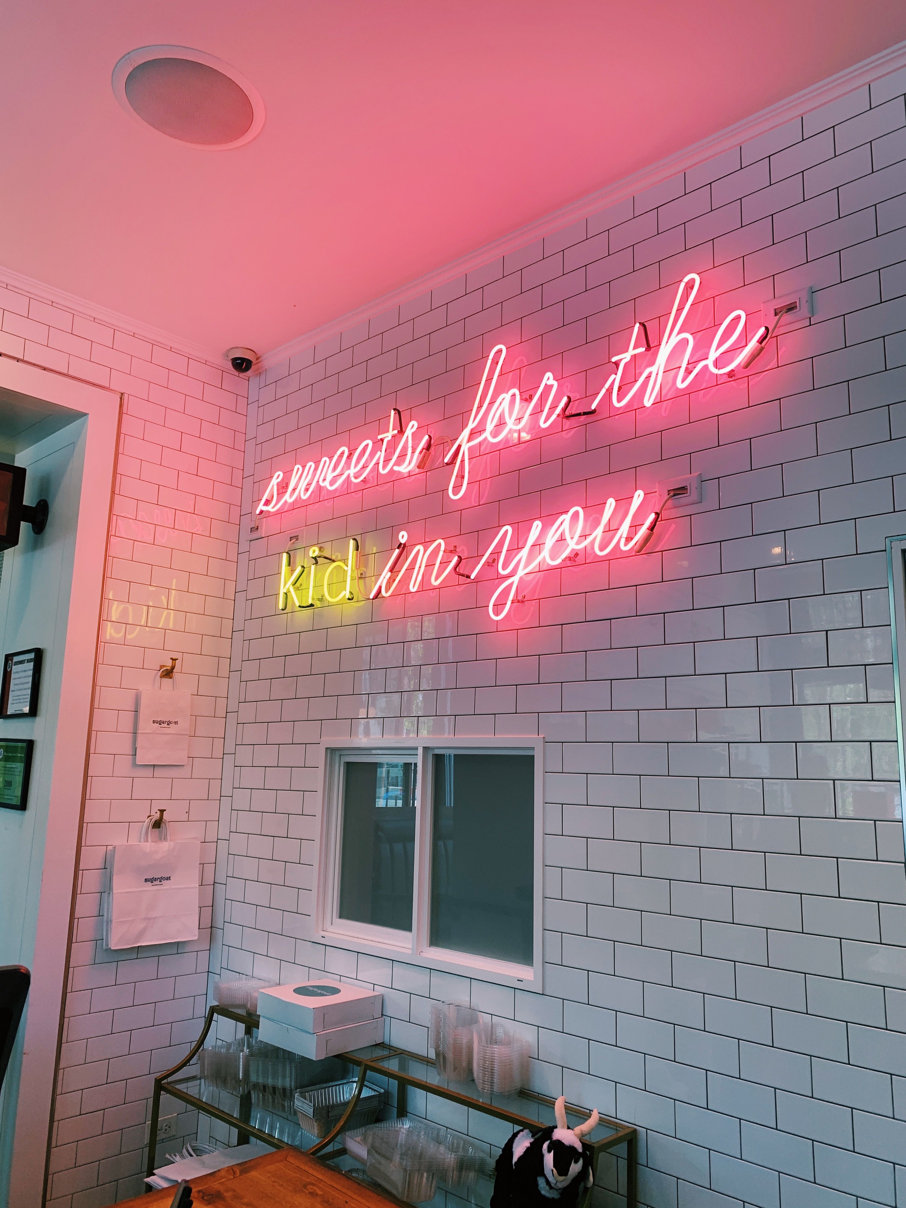 A neon sign that says "Sweets for the kid in you" in pink and yellow
