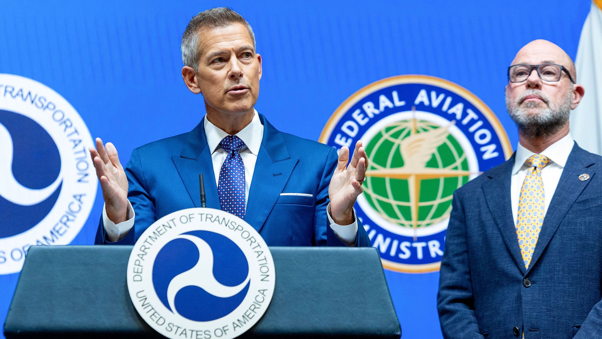 A gray-haired Transportation Secretary Sean Duffy, wearing a navy suit, white shirt and blue tie with white dots, gestures before a podium with a DOT sign on it, as a bespectacled, bald FAA Administrator Bryan Bedford stares ahead while wearing a navy suit, cream shirt and yellow tie with blue dots