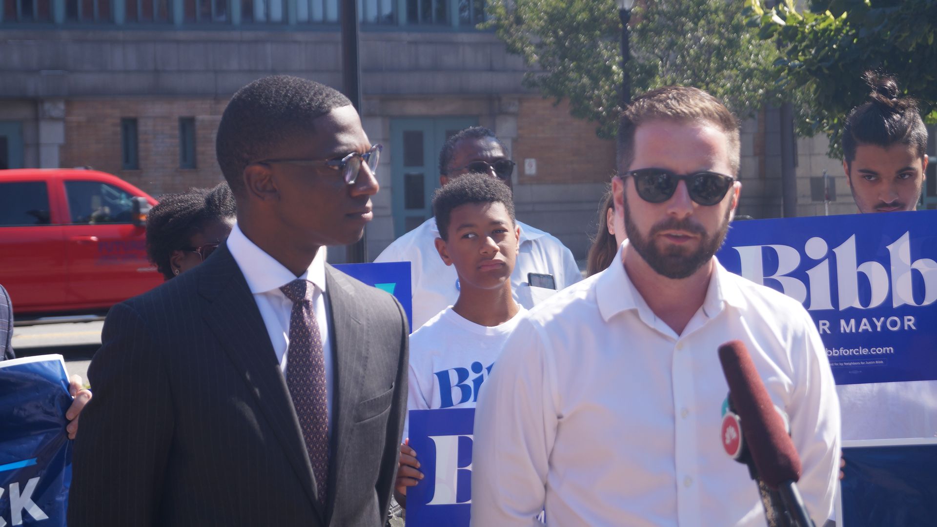 A black man in suit next to a white man in sunglasses and white shirt