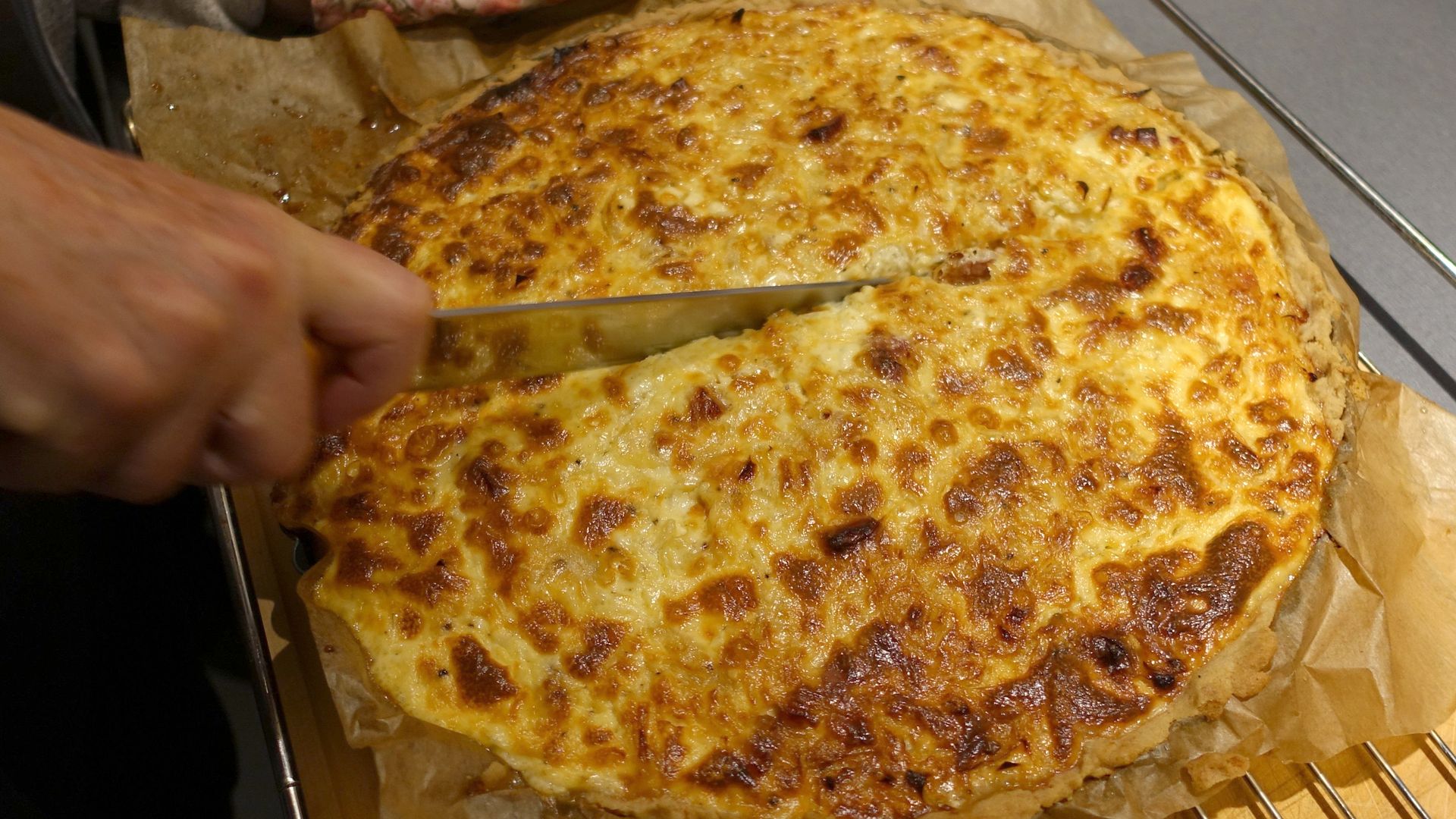 A hand holding a knife cuts into an onion cake. 