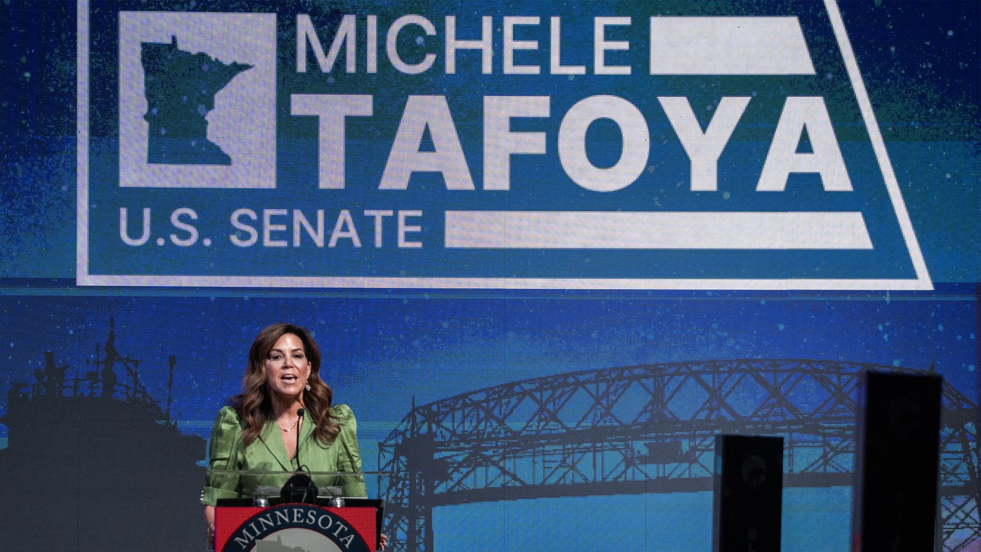 Michelle Tafoya in a green jacket at a minnesota republican party podium with the words Tafoya U.S. Senate behind her