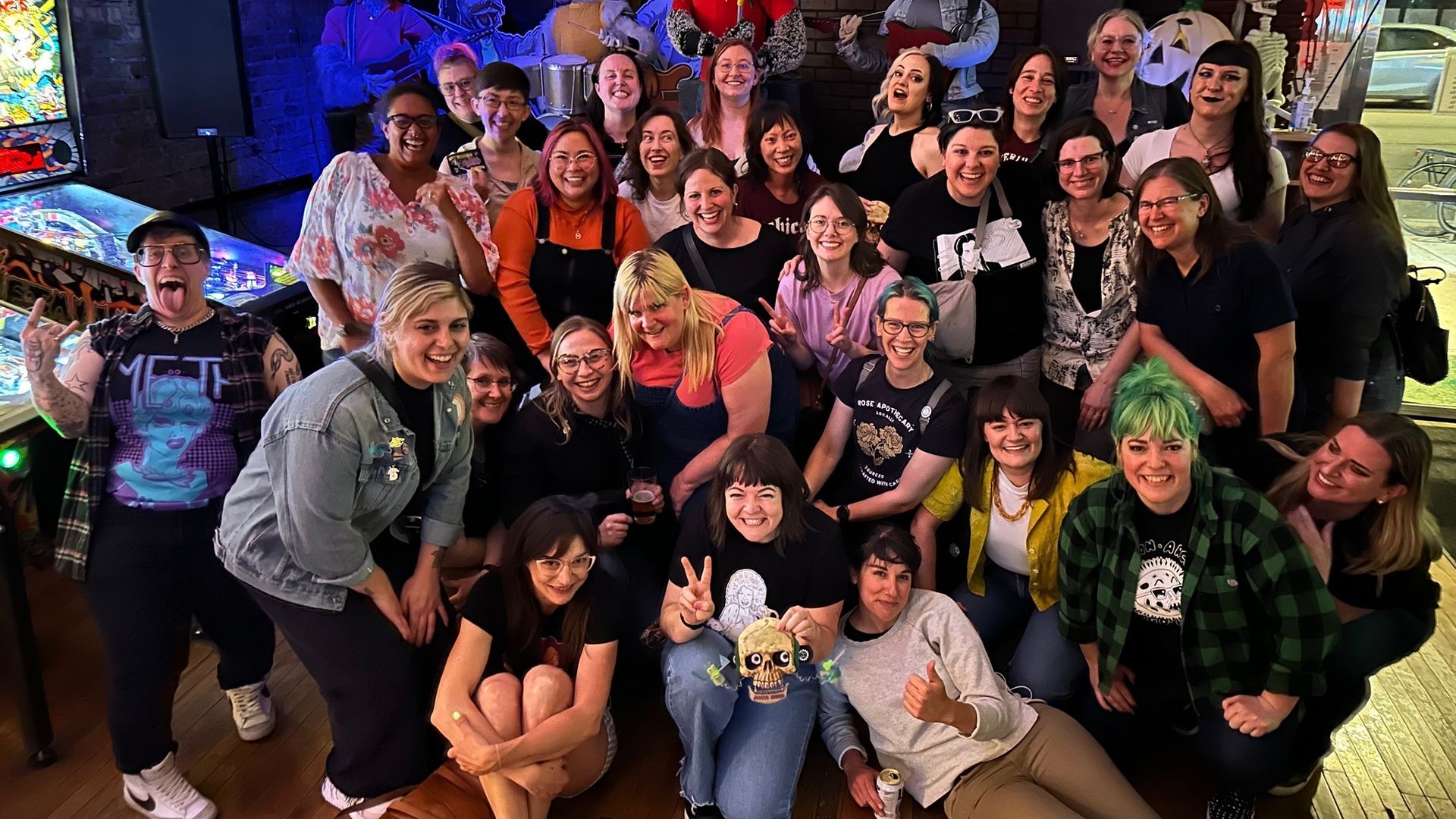 Group of people gathered together with pinball machines in background.