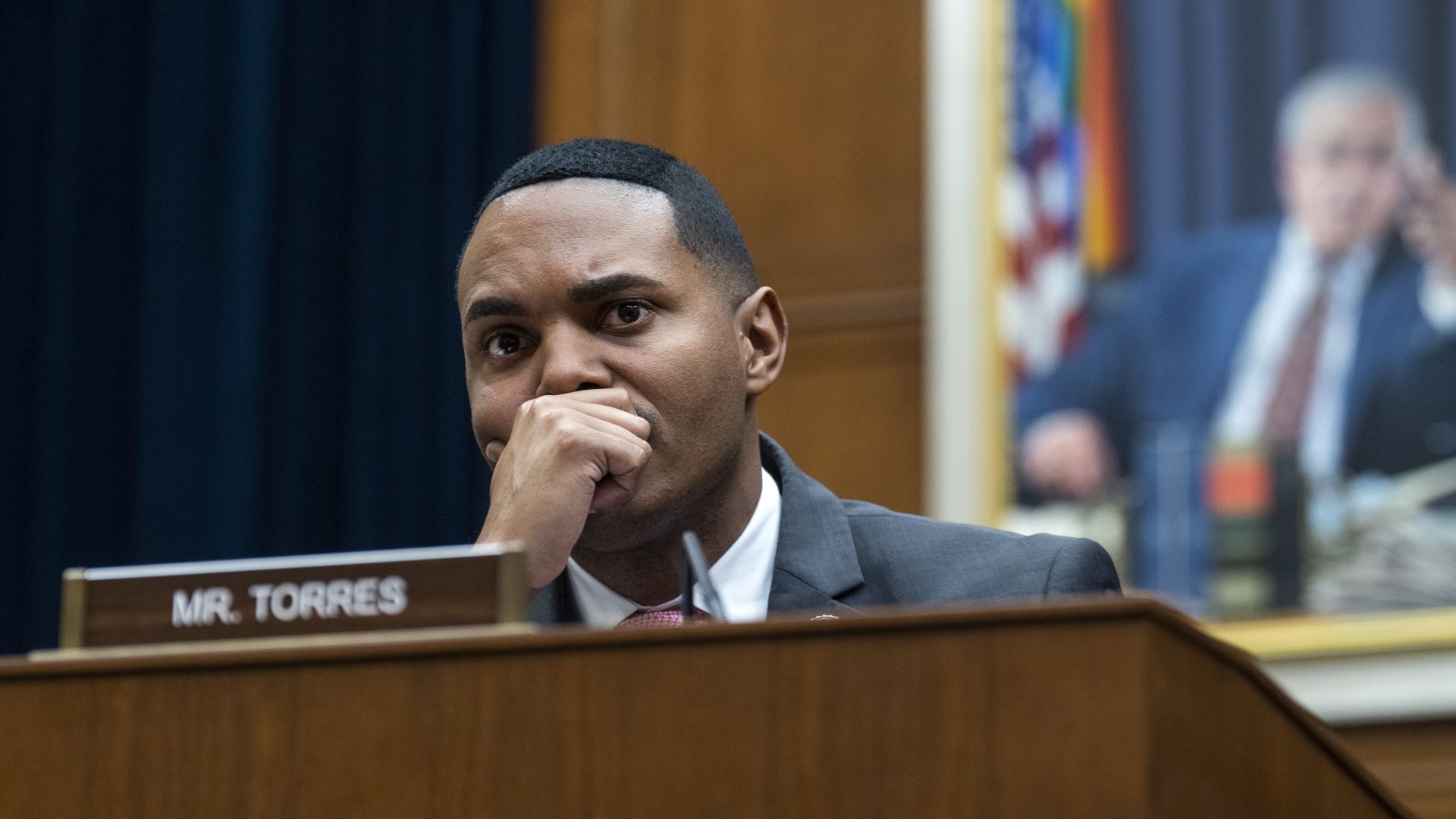 Rep. Ritchie Torres, wearing a gray suit, with his hand over his mouth, sitting at a committee dais behind a placard that says "Mr. Torres"