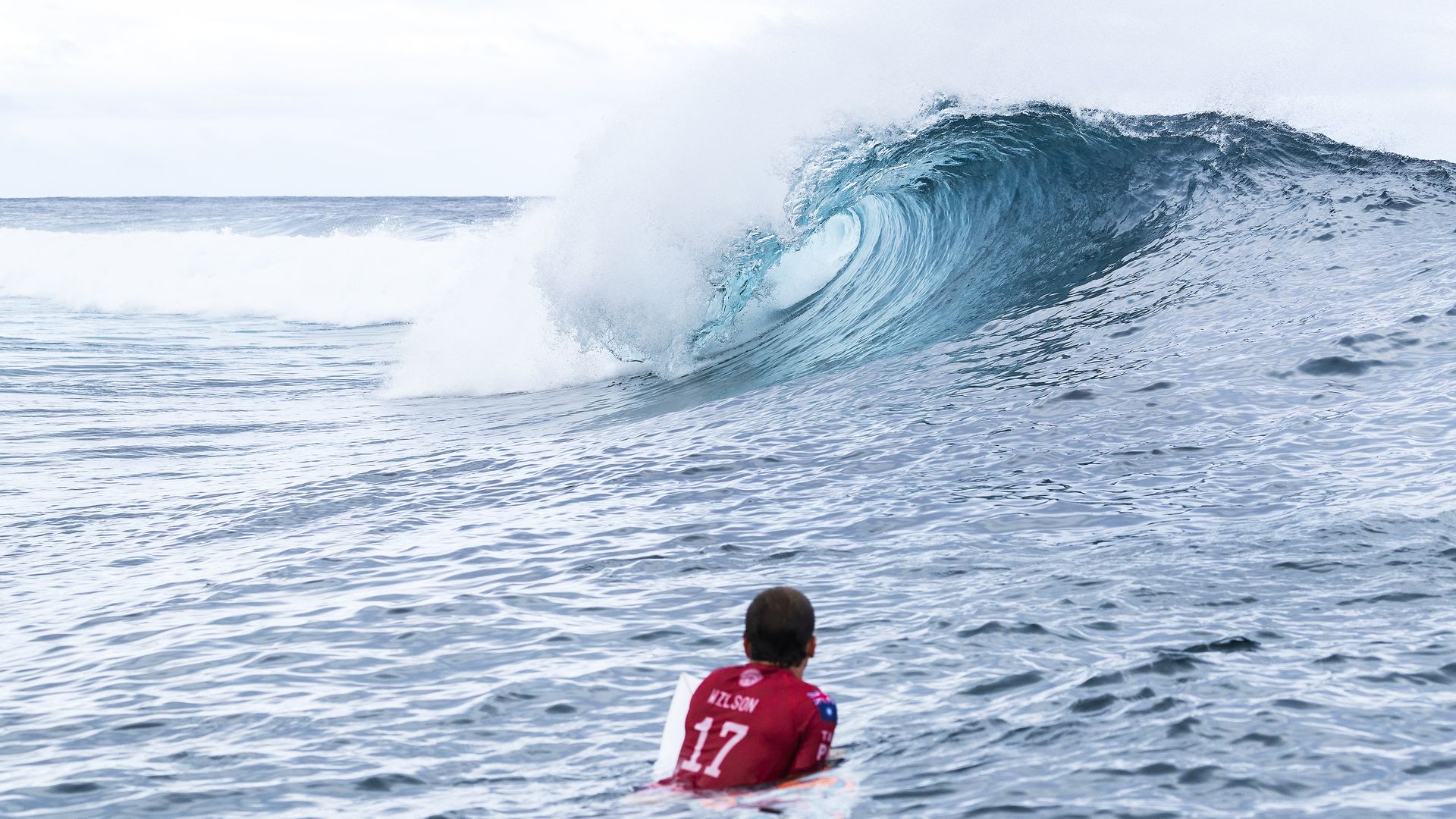 In this image, a surfer drifts on a board and watches a wave crash in front of him.