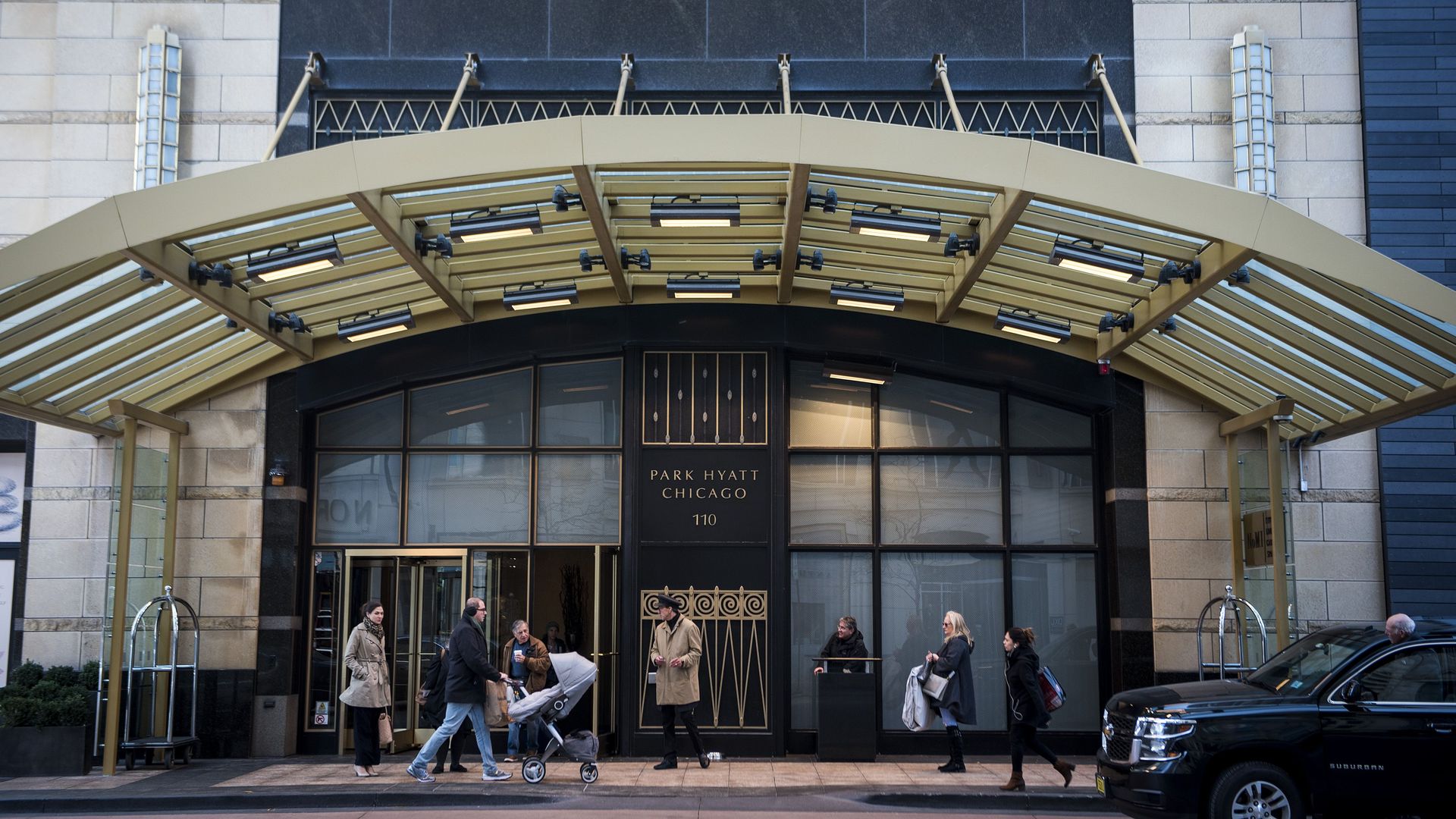 People walk outside the Park Hyatt Chicago, wearing coats. One couple pushes a stroller.