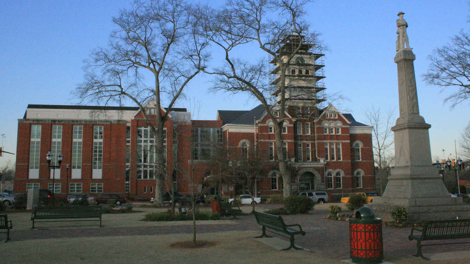 A photo of a tall Confederate monument with a man in a hat atop in a courthouse square