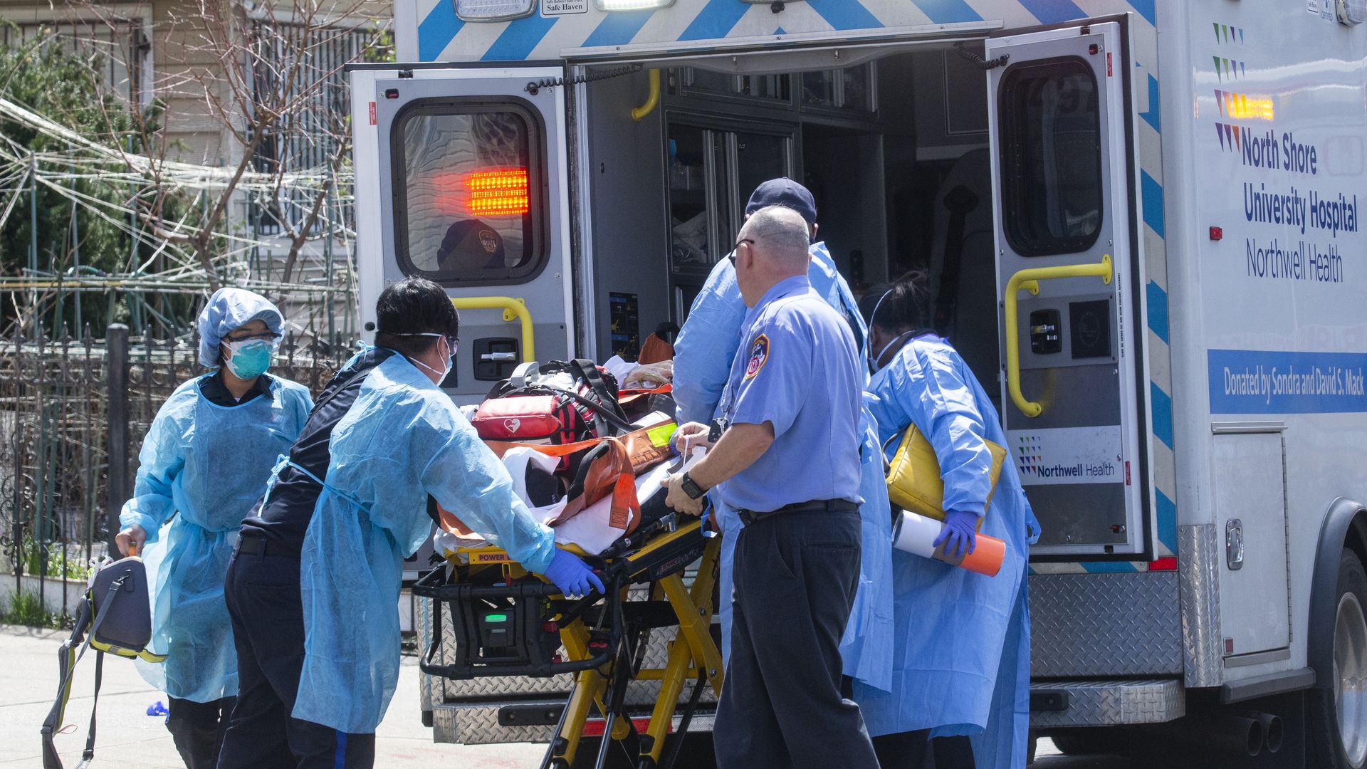 Medics in blue gowns load a coronavirus patient onto a stretcher and into an ambulance.