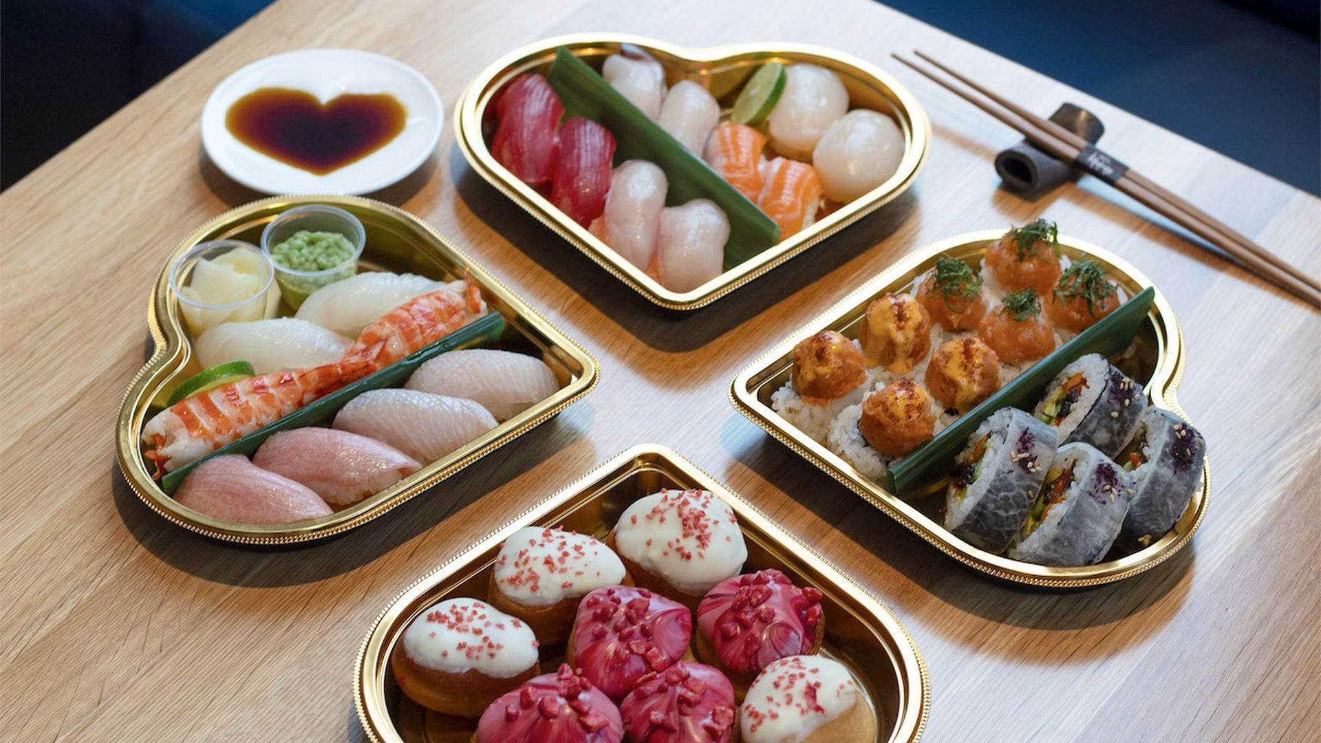 A set of four heart-shaped boxes filled with sushi on a light wood table