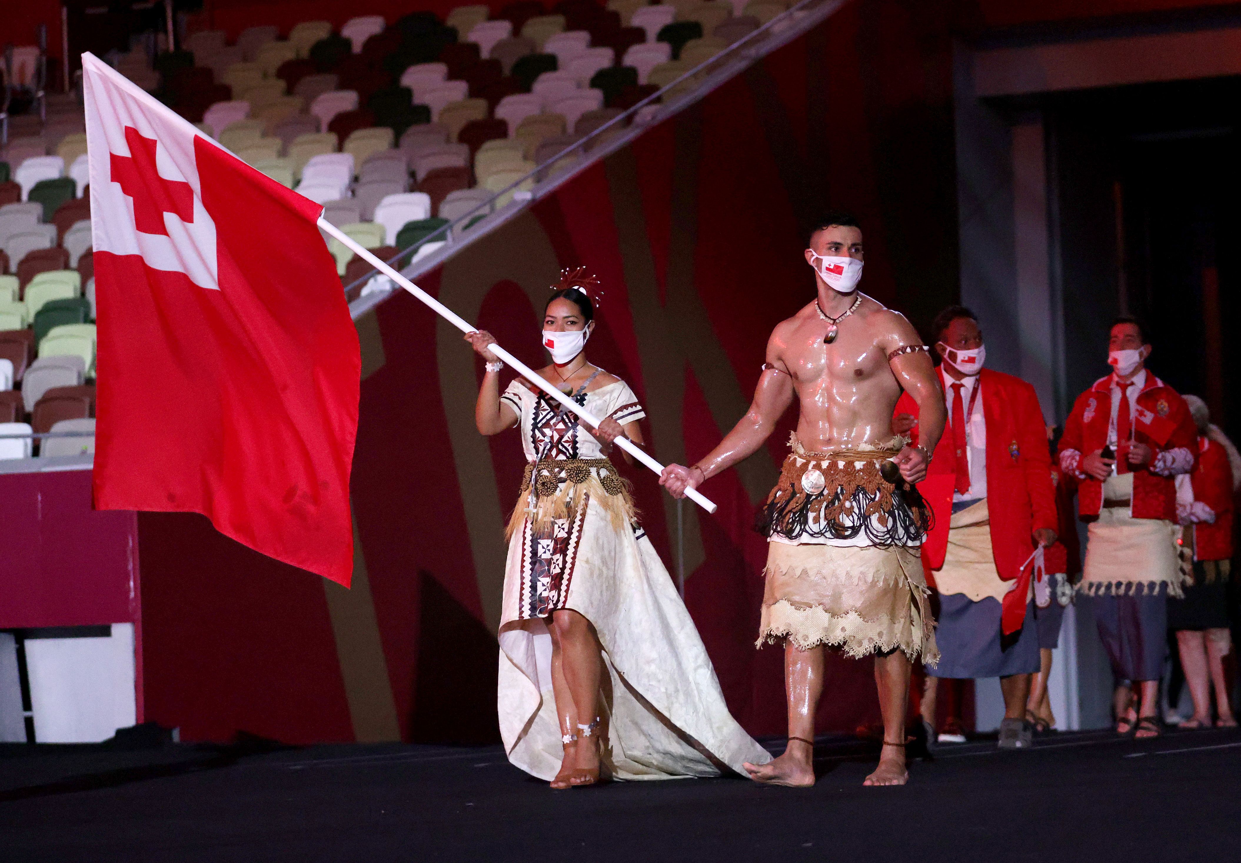 Picture of the Team Tonga flag bearers, the man is shirtless and his torso is covered in oil 