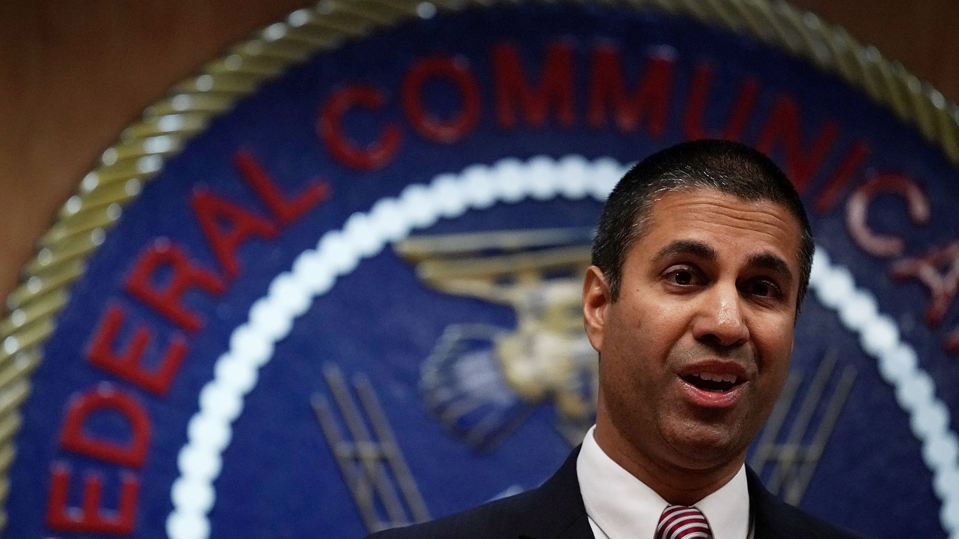 FCC Chairman Ajit Pai standing before the FCC seal.