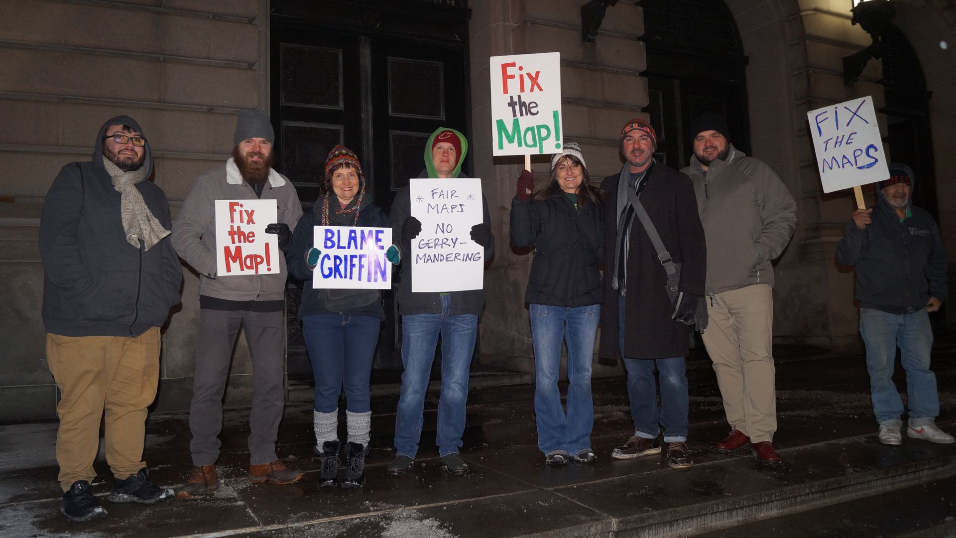 A small group of protesters in winter clothes holding signs advocating for fair maps.