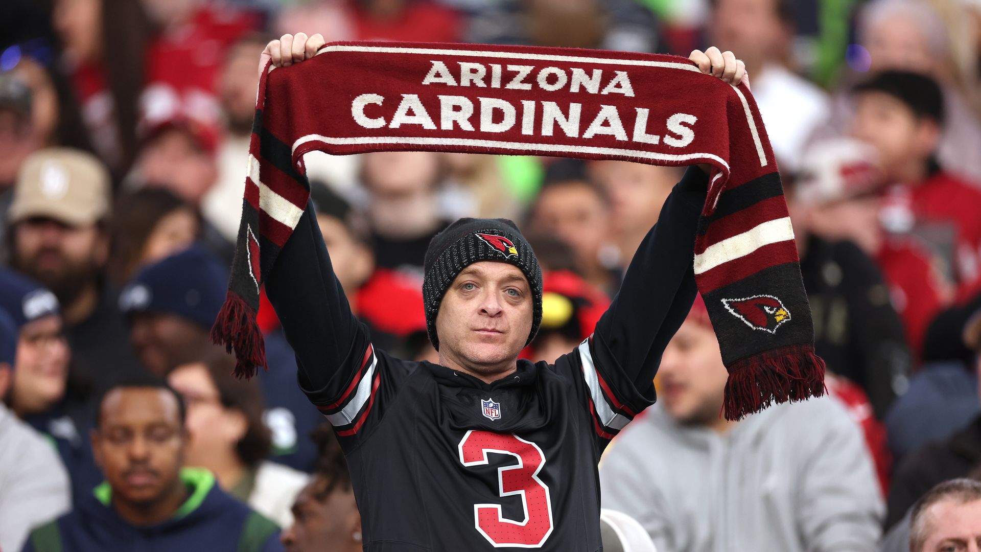 A fan holds up an Arizona Cardinals scarf in the stands at a football game. 