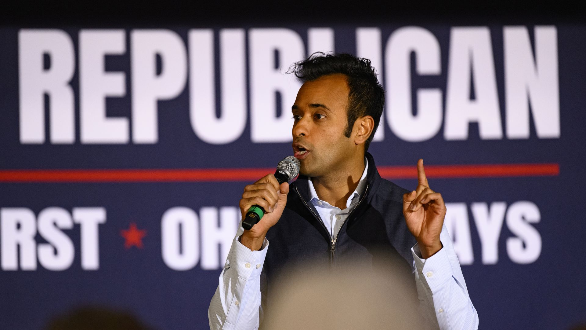 Vivek Ramaswamy speaks into a microphone in front of a large sign that says "Republican"