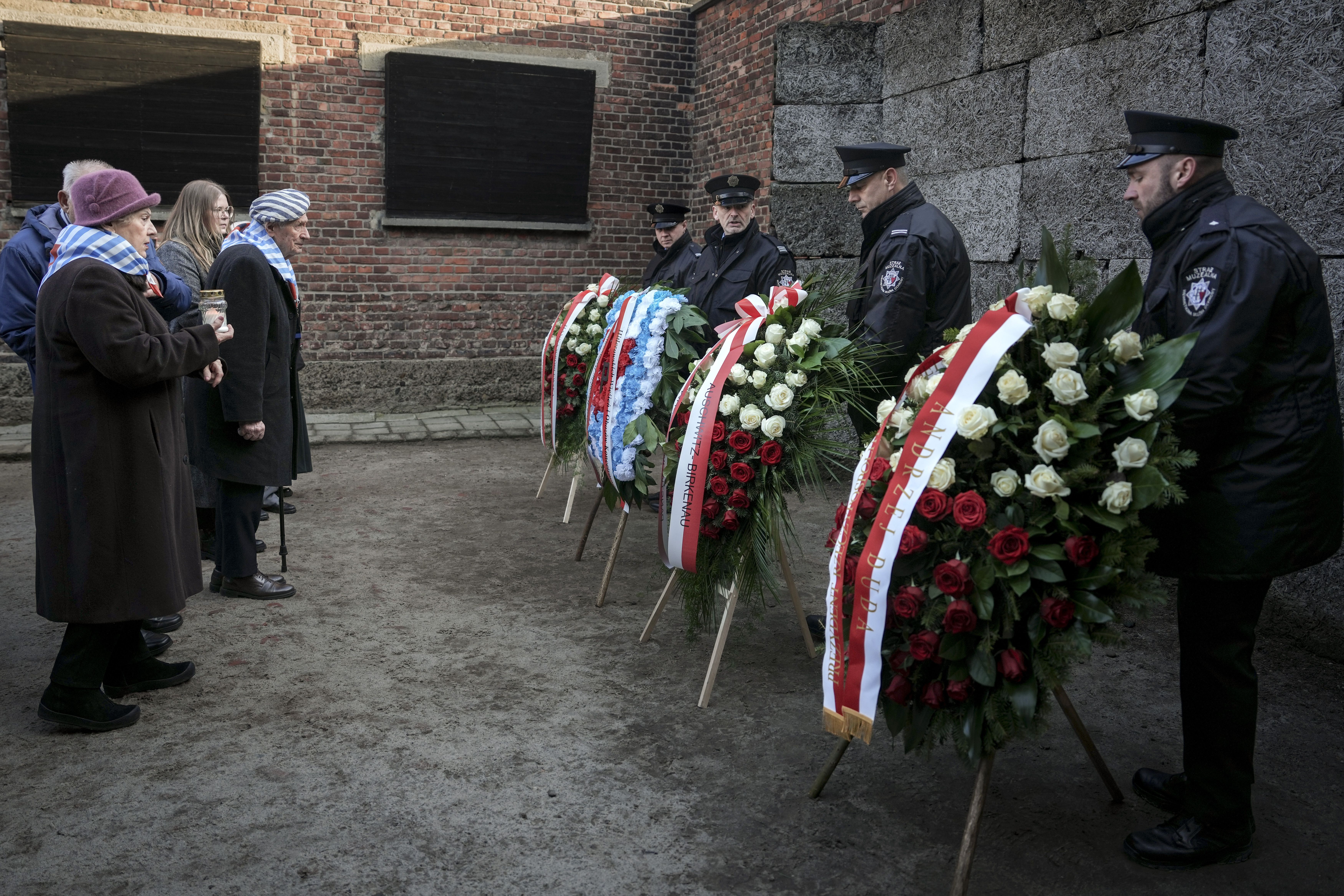 Museum security staff handle wreaths as survivors and relatives stand at the Death Wall during a ceremony marking the 80th anniversary of the liberation of the Auschwitz-Birkenau former Nazi German concentration and extermination camp, in Oswiecim, Poland, Monday, Jan. 27. 2025.(AP Photo/Oded Balilt