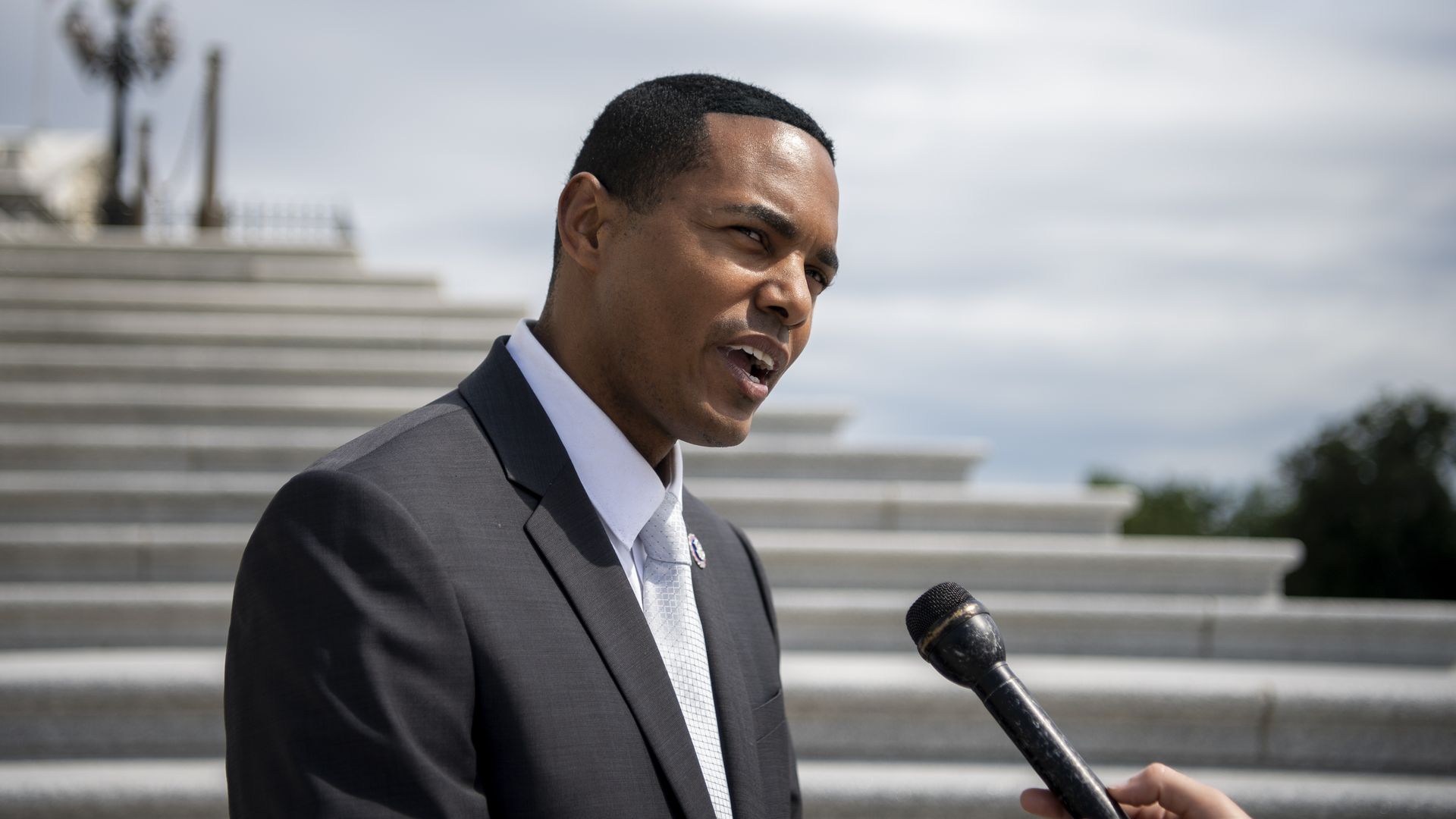 Rep. Ritchie Torres, wearing a gray suit and speaking into a microphone in front of the U.S. Capitol's white marble steps.