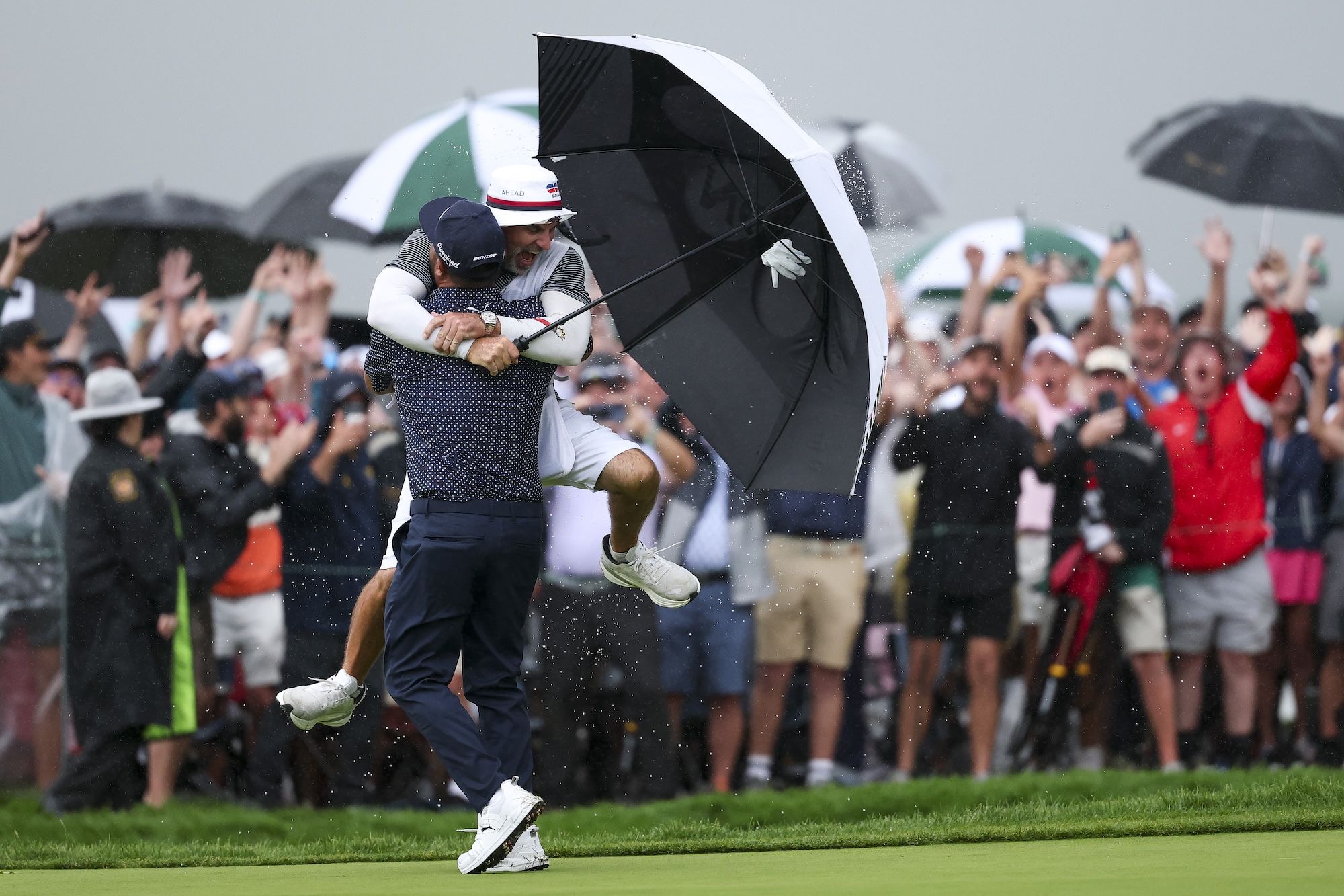 A caddie with an umbrella in hand jumps into a golfer's arms in celebration. 
