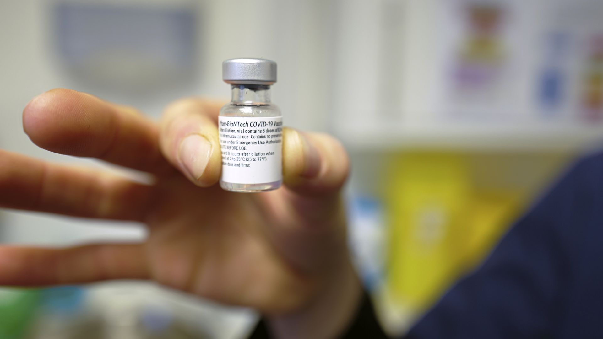A hand holds a vial of the COVID vaccine up to the camera