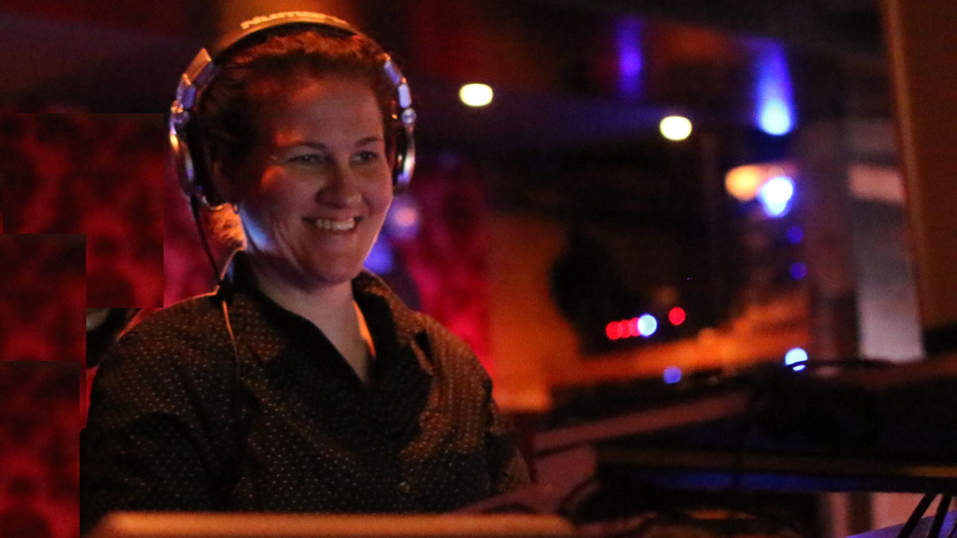 Jenna Jordan, wearing headphones, smiles as she looks at a sound mixing board.