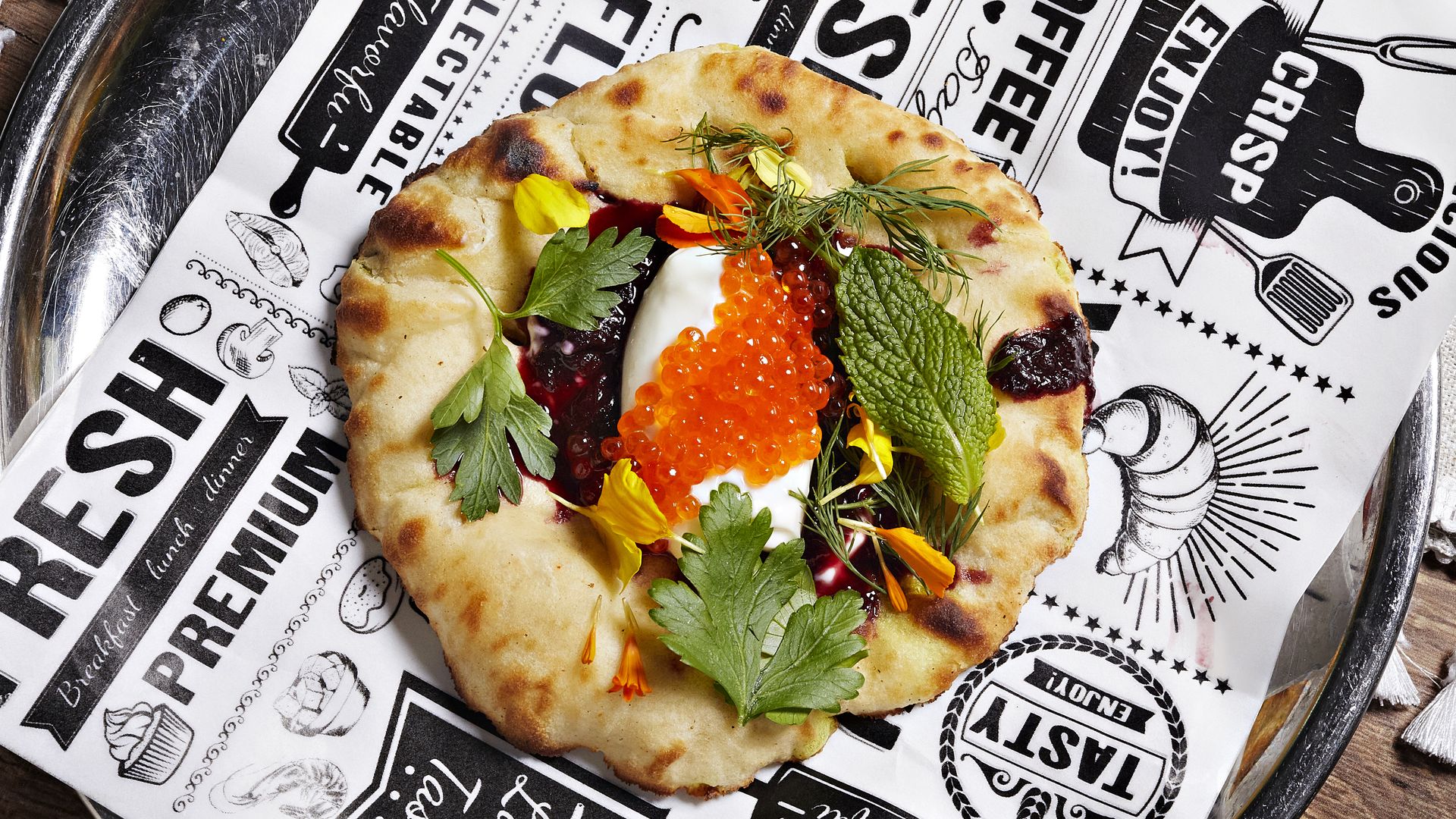 An Indian kulcha on paper topped with herbs and trout roe
