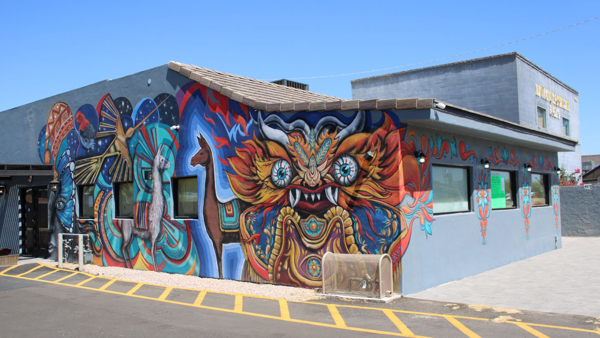 A building with a colorful mural that features llamas and an orange creature with large eyes, horns and pointed teeth.