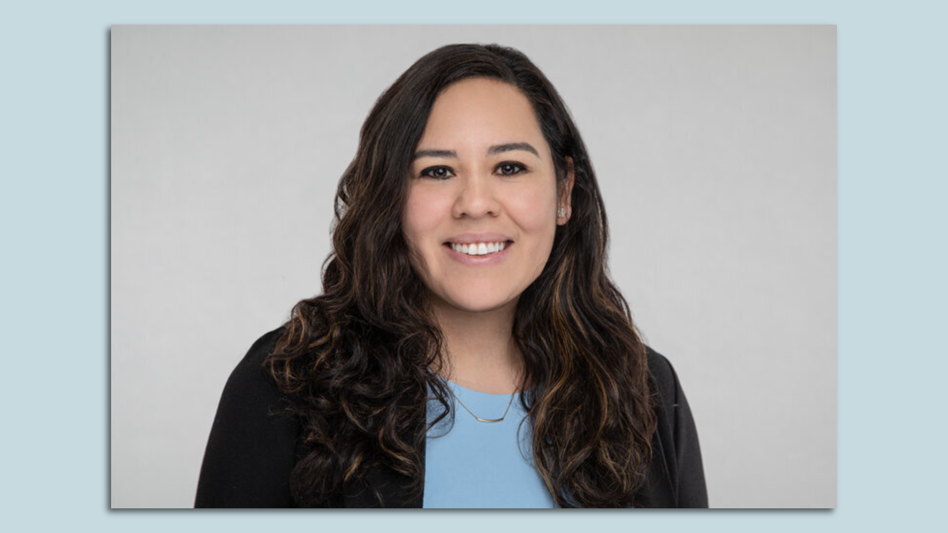 Rosamaria Cristello smiles for a portrait, against a light blue backdrop