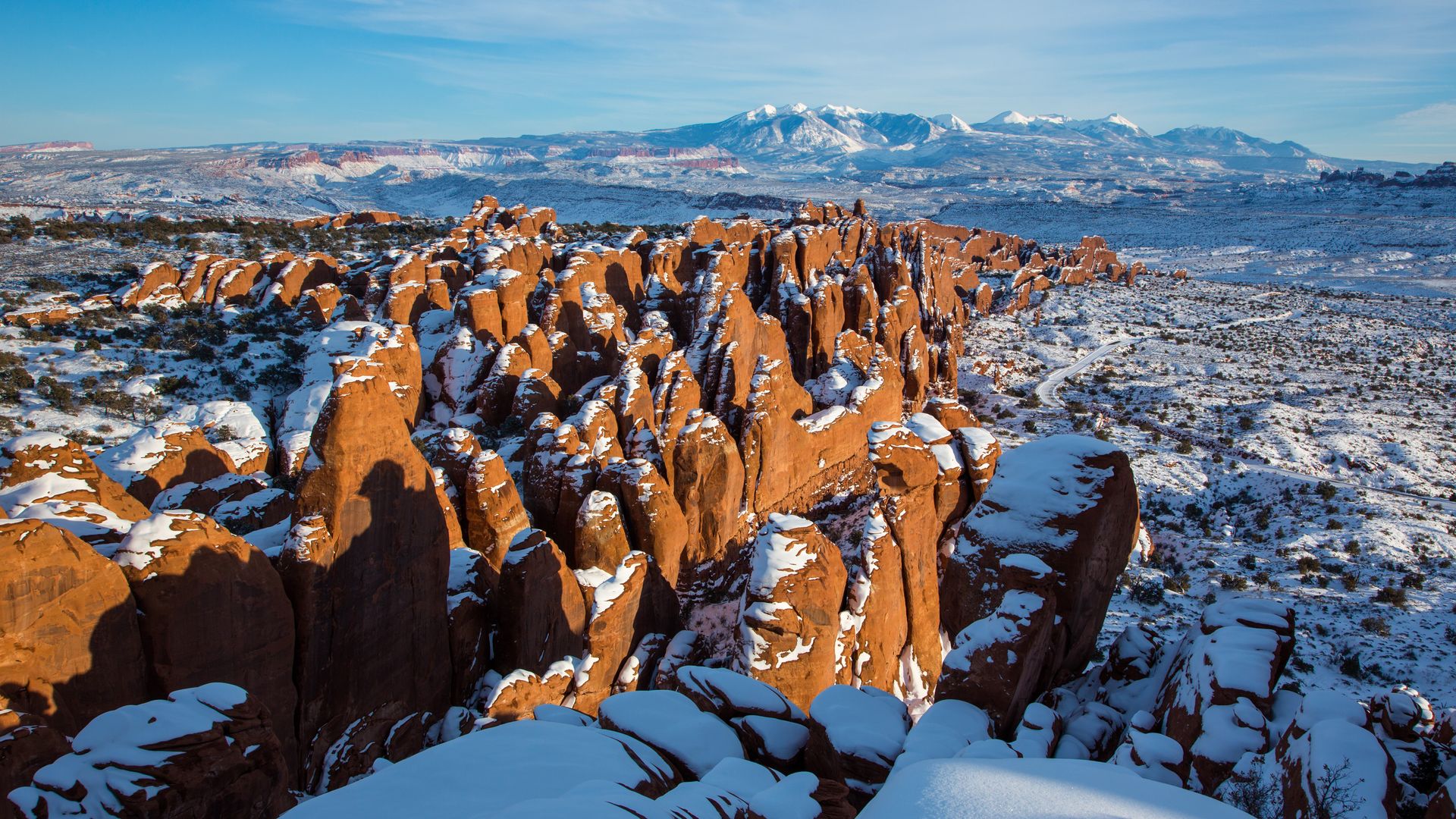 Red rock fins in a cluster on a snowy desert landscape with mountains in the background.