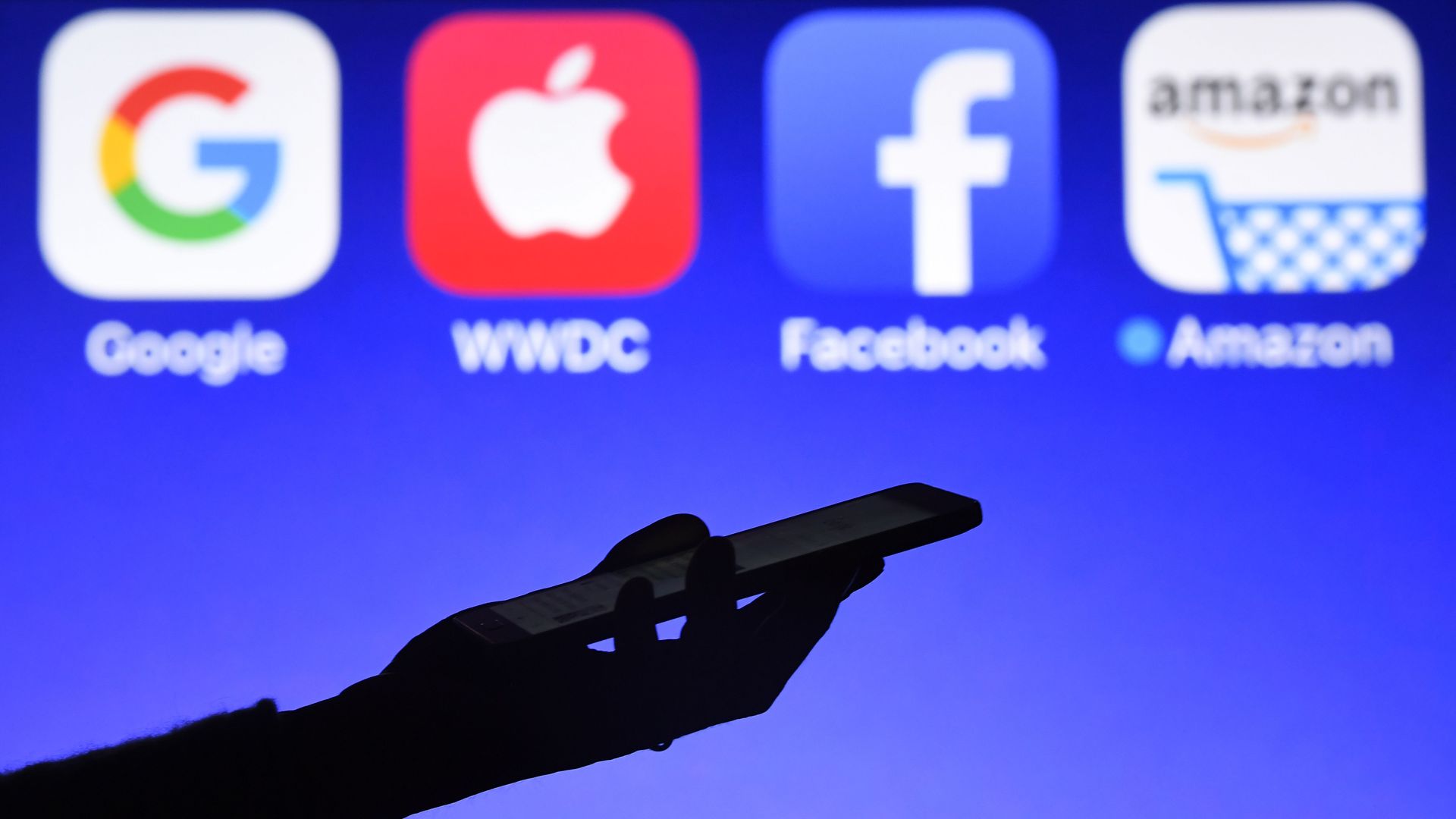 A phone held in front of Big Tech logos