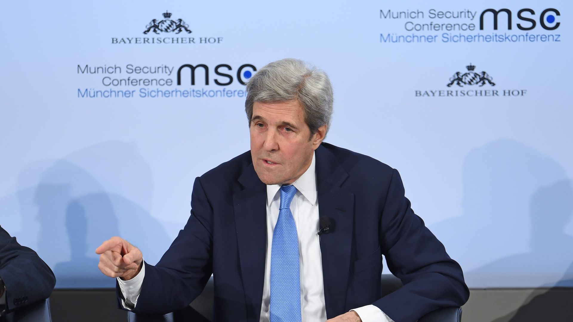 Kerry gestures while speaking, seated, on stage