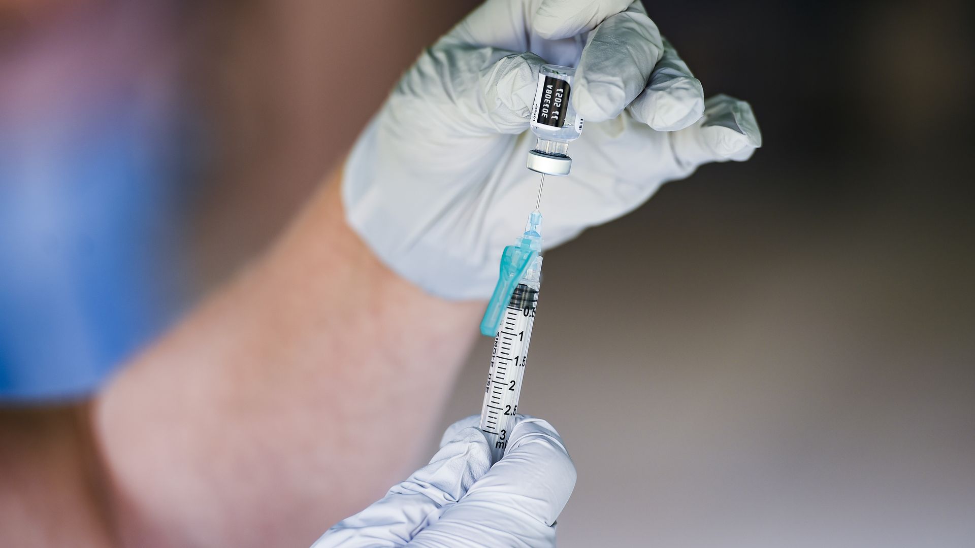 Picture of two hands wearing medical gloves filling a syringe with the COVID-19 vaccine