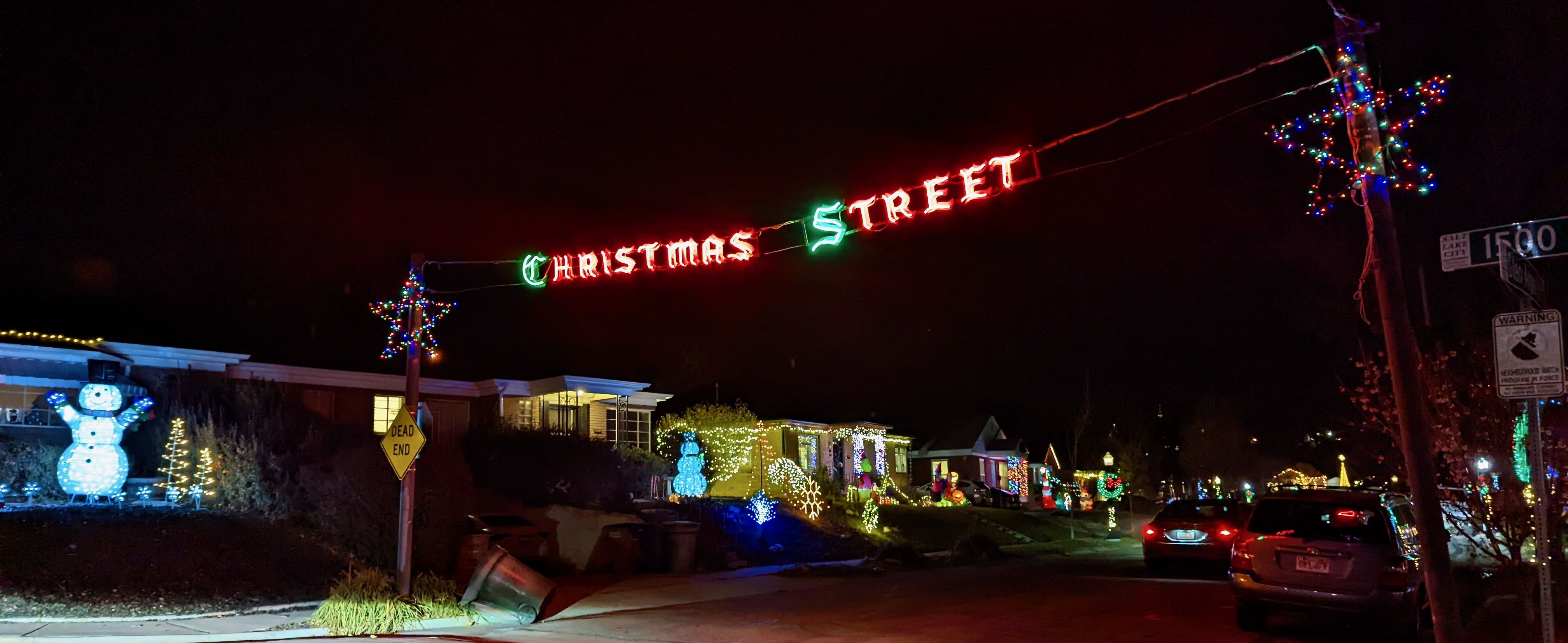 A street with houses decorated for Christmas and a lighted sign that reads "Christmas Street" hanging over it.
