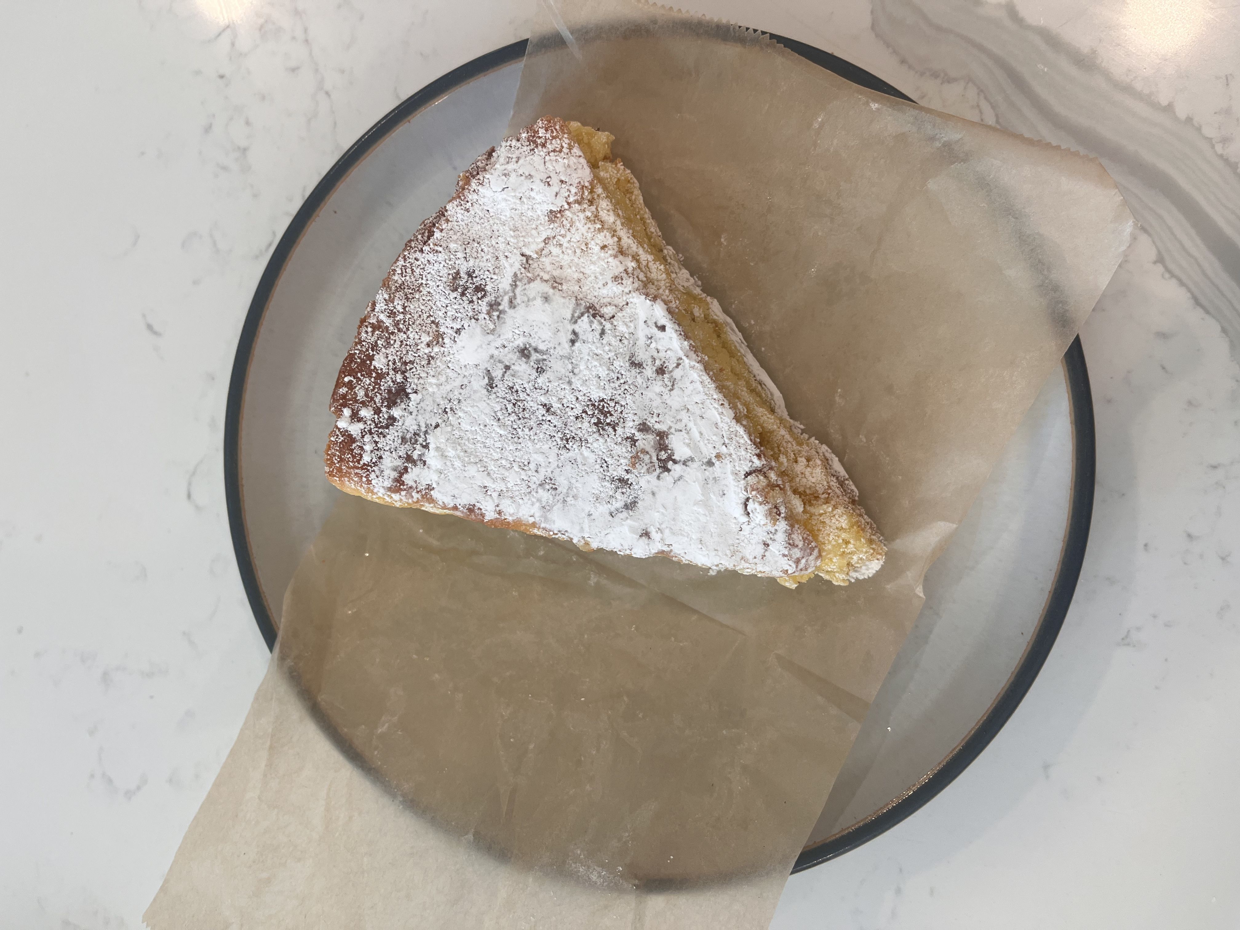 A triangular slice of almond cake dusted with powdered sugar on parchment paper.