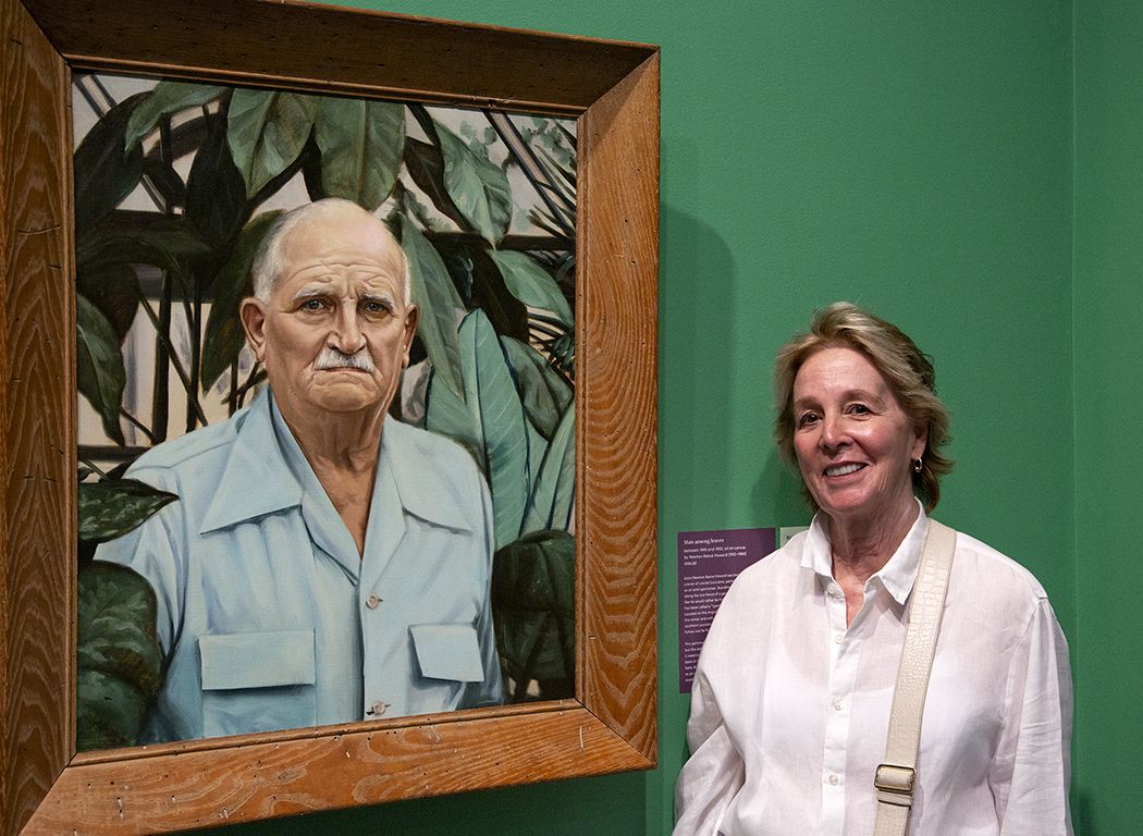 A photo of Karen Kraak Wood standing next to a portrait of her grandfather, Henry Kraak.
