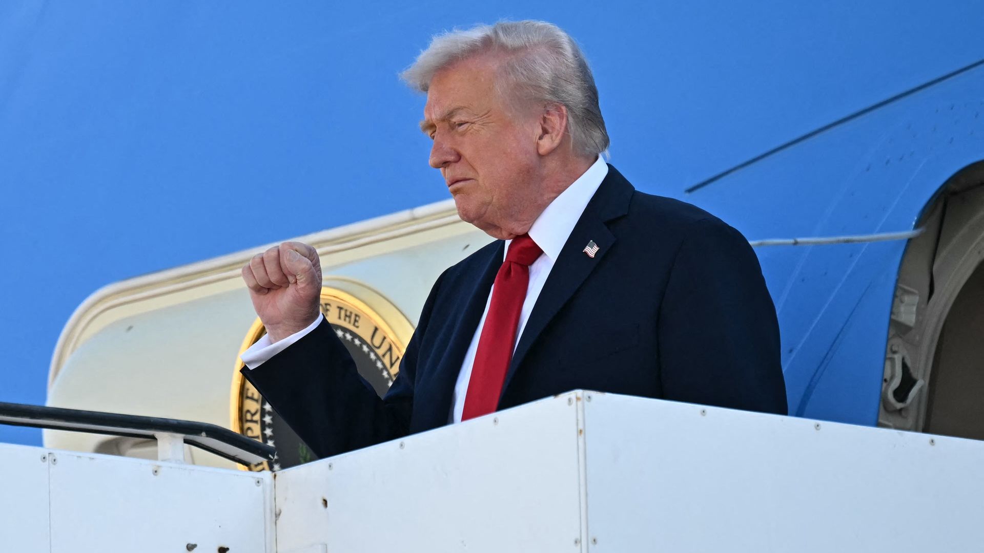 President Trump,  wearing a navy jacket with a US flag pin, white shirt and red tie, gestures as he disembarks from Air Force One upon arrival at Ben Gurion Airport on the outskirts of Lod near Tel Aviv on October 13, 2025, 