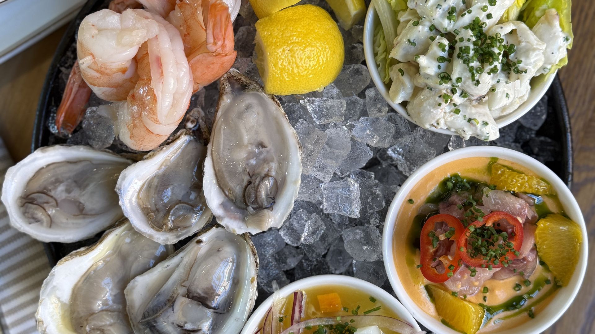 Seafood platter on ice with oysters, shrimp, lemon wedges, and a lettuce cup of creamy seafood salad; side bowls of sauces and a corn chips bowl.